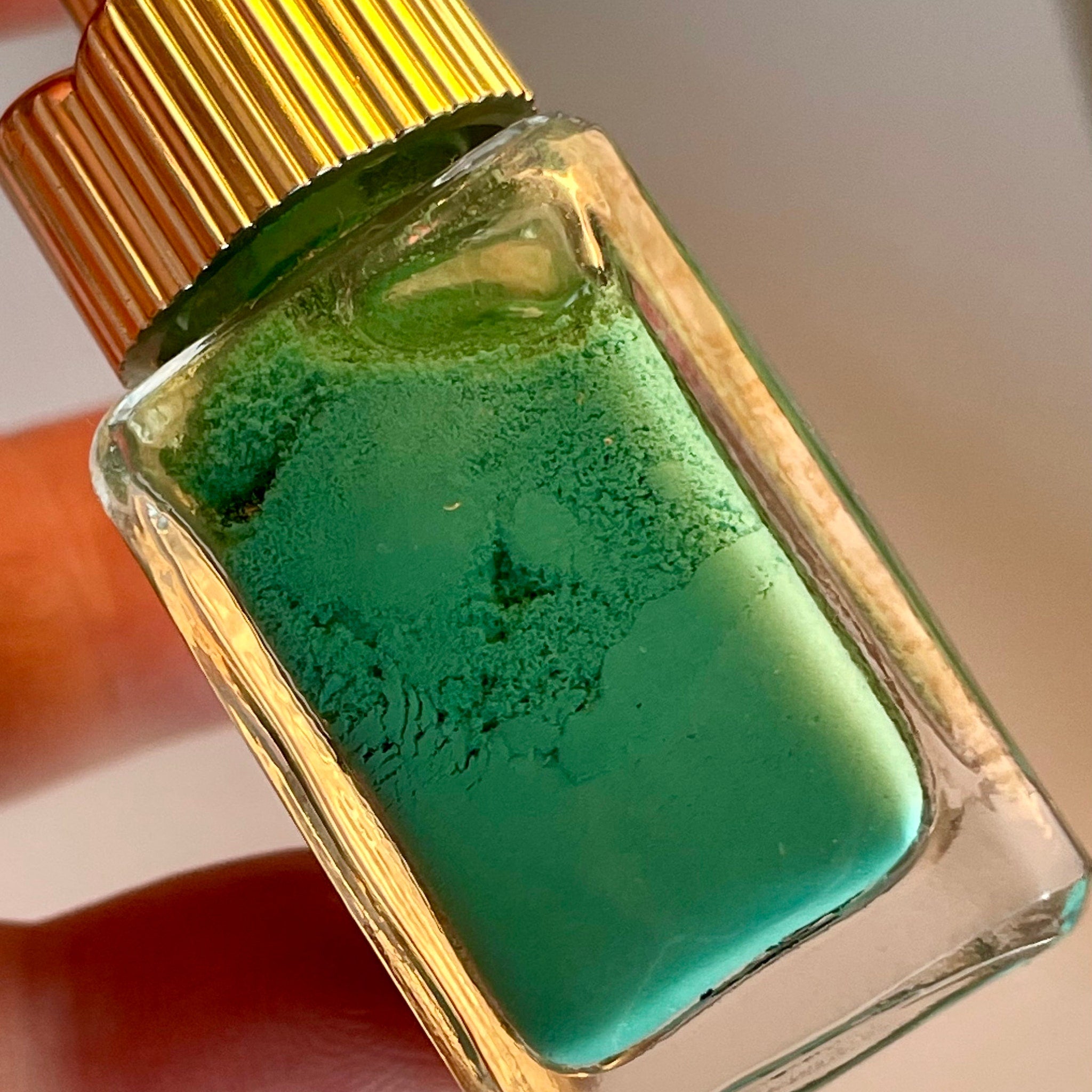 Vintage 1960 Maybelline green eyeliner bottle displayed at an angle, highlighting golden spire lid and glass bottle sheen