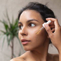Facial serum application, woman with dark hair, white dropper, yellow liquid being applied to face