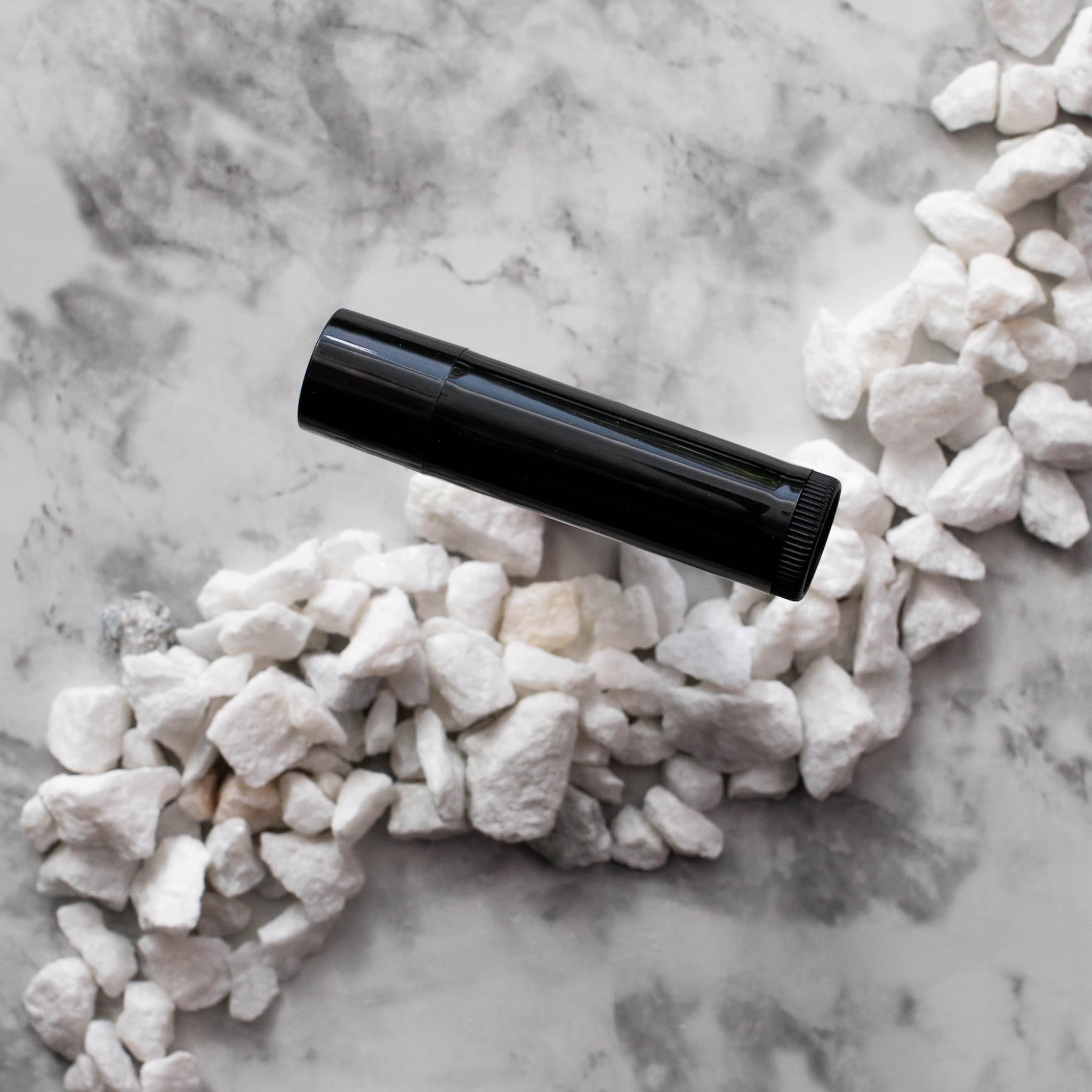 Black tube with glossy finish, on white marble and white stones, product shot