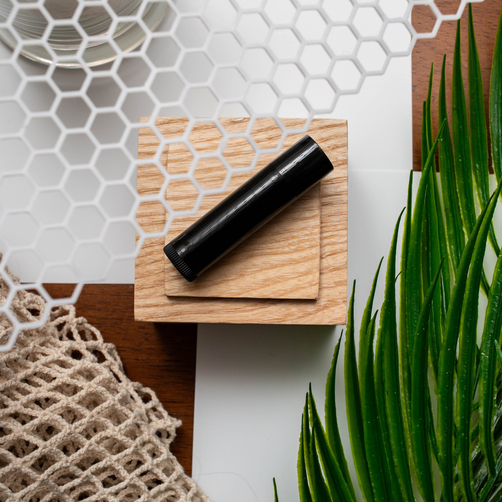 Black lip balm on wood block with green leaves and honeycomb pattern background