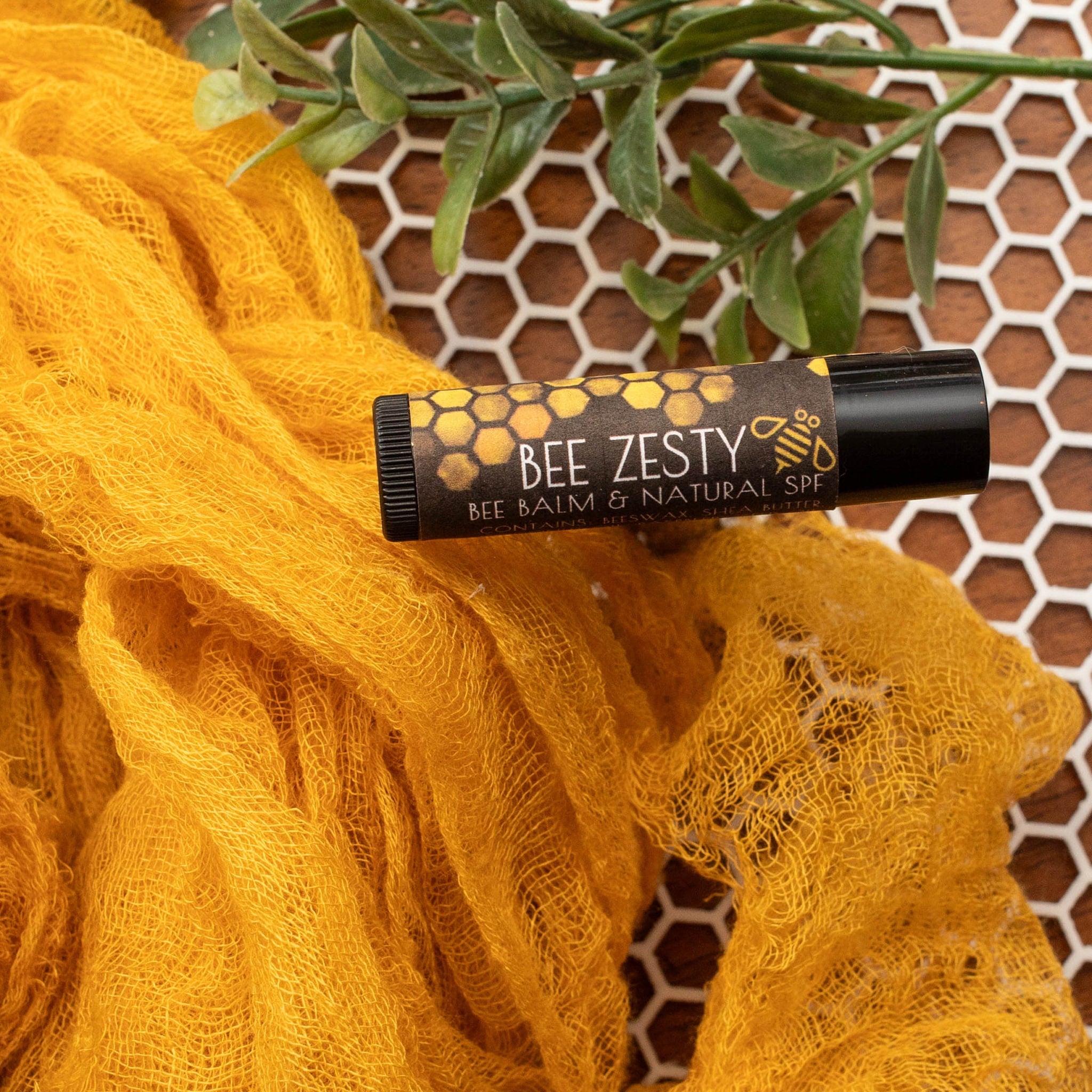 Lip balm tube with black and gold label, yellow fabric, and honeycomb pattern background