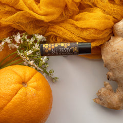 Lip balm tube with black cap, Bee Zesty label, and orange fruit on white background