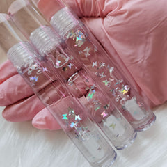 Lip gloss tubes with clear plastic, butterfly glitter, and pink lid, held in gloved hand.