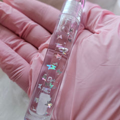 Lip gloss tube with clear liquid, butterfly glitter, and pink background of fabric