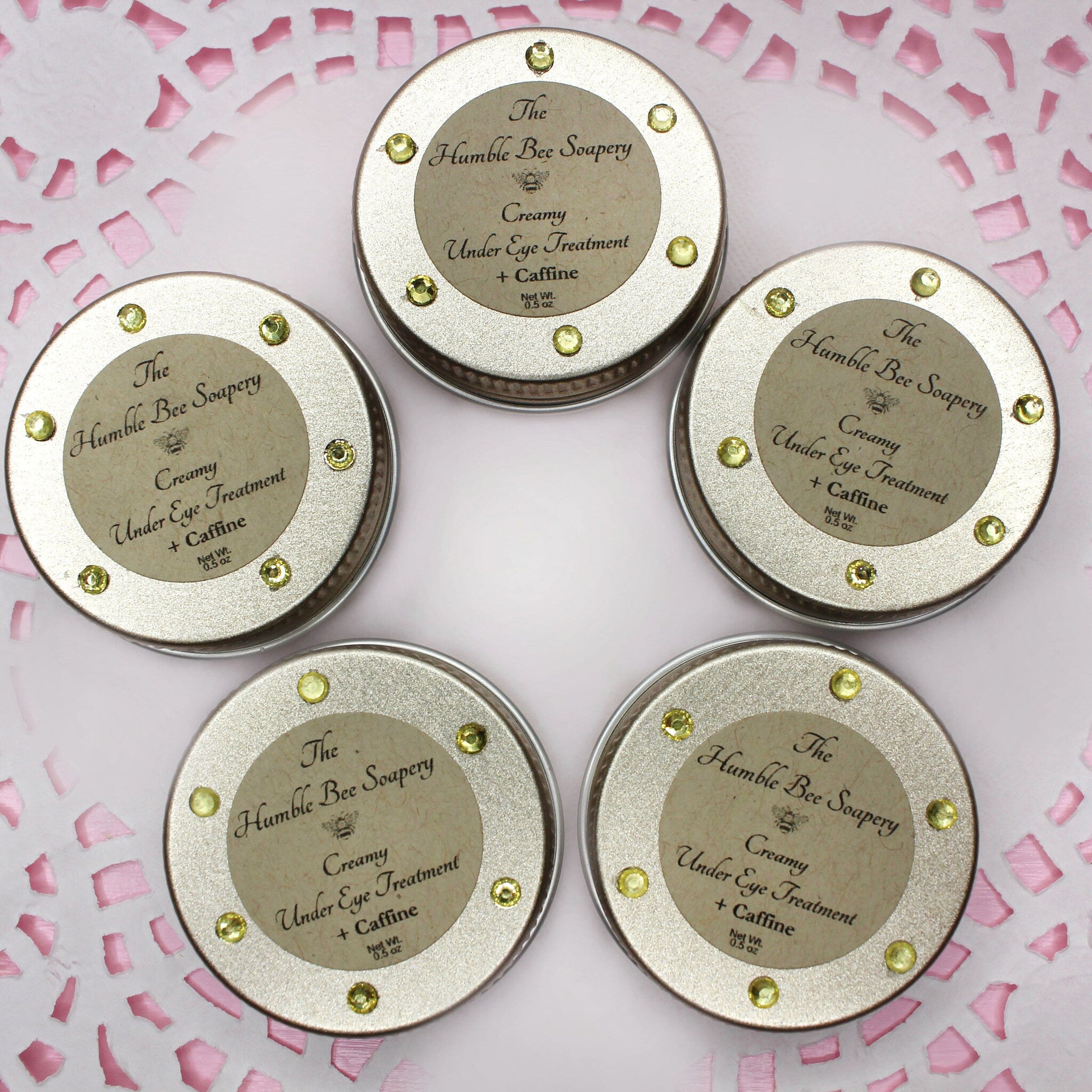 Under eye treatment in silver tins with yellow gems and The Humble Bee Soapery label on pink background