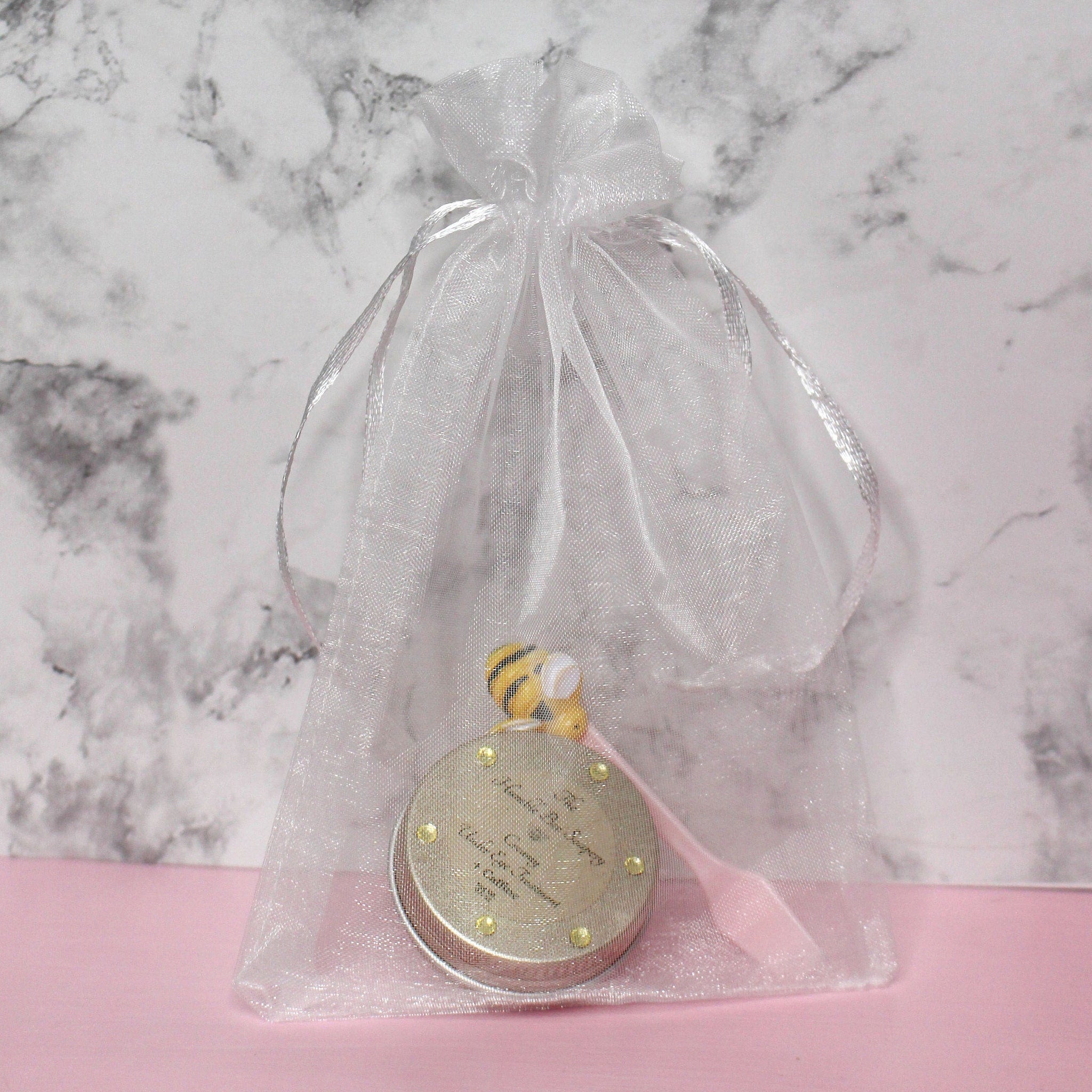 Gift bag with white sheer material, silver ribbon tie, and gold-trimmed container inside