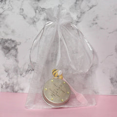 Gift bag with white sheer material, silver ribbon tie, and gold-trimmed container inside