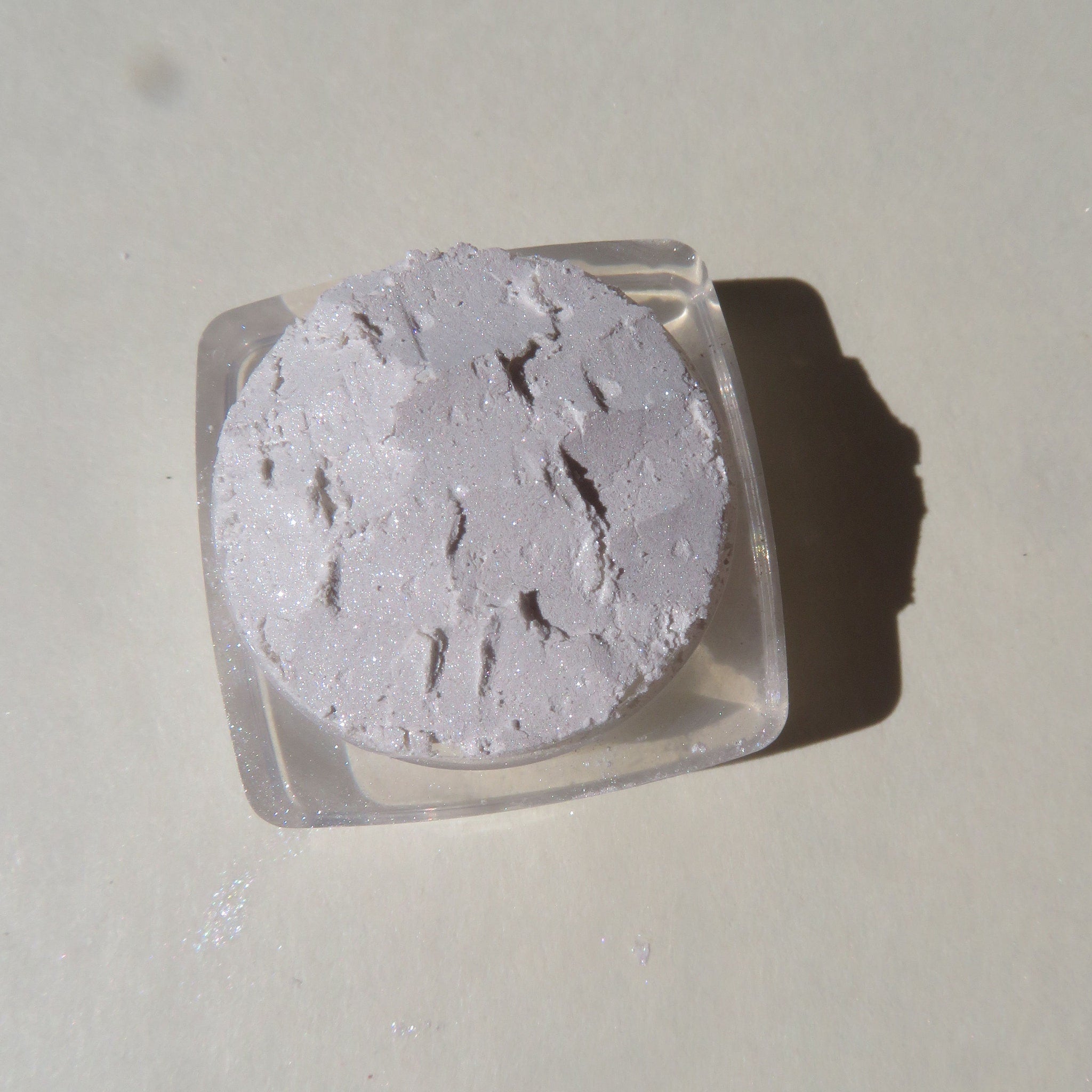 Close-up of soft white mineral eyeshadow jar with shimmer powder and gold lid on marble surface