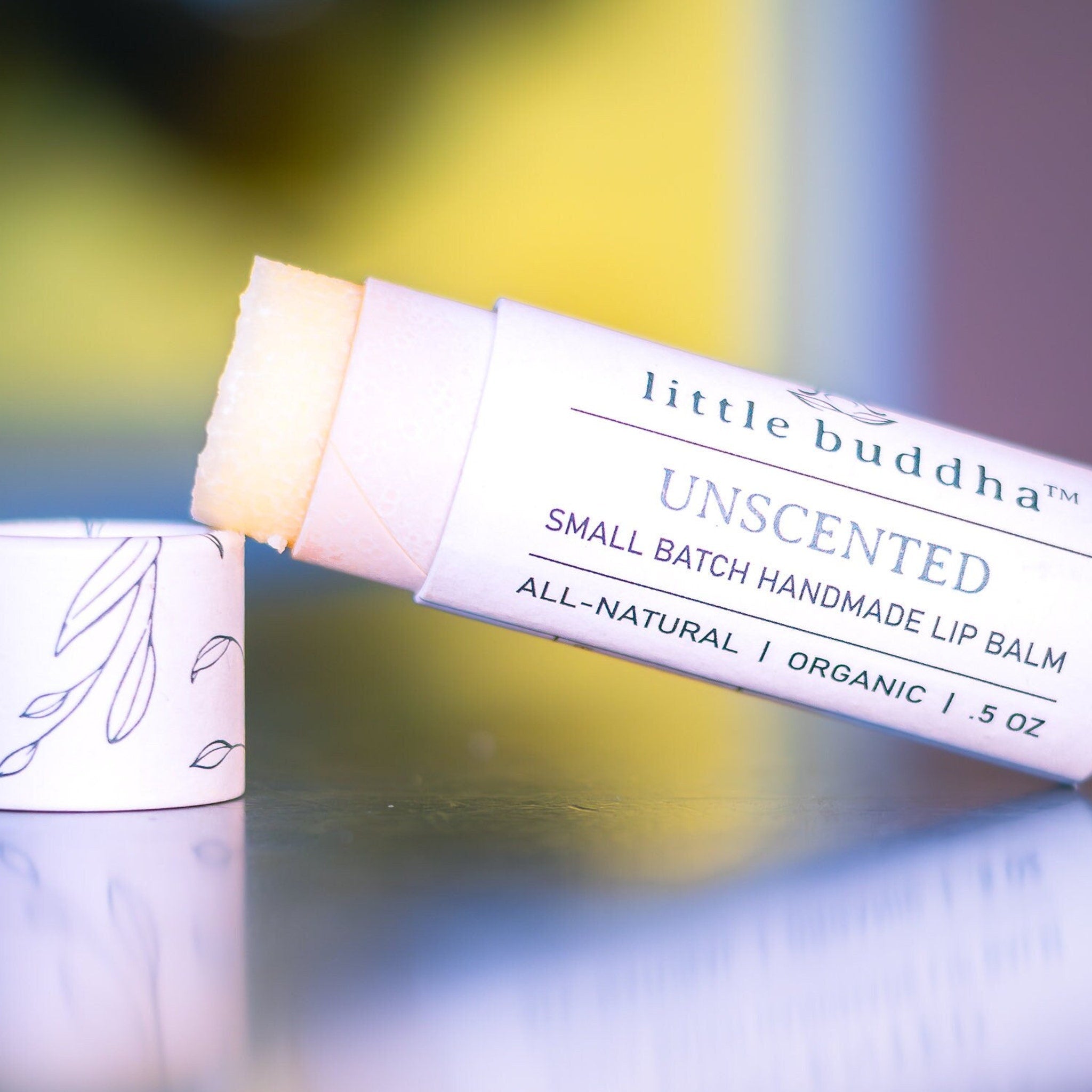 Lip balm tube with white paper, leaf pattern, and Little Buddha branding, showing lip balm stick