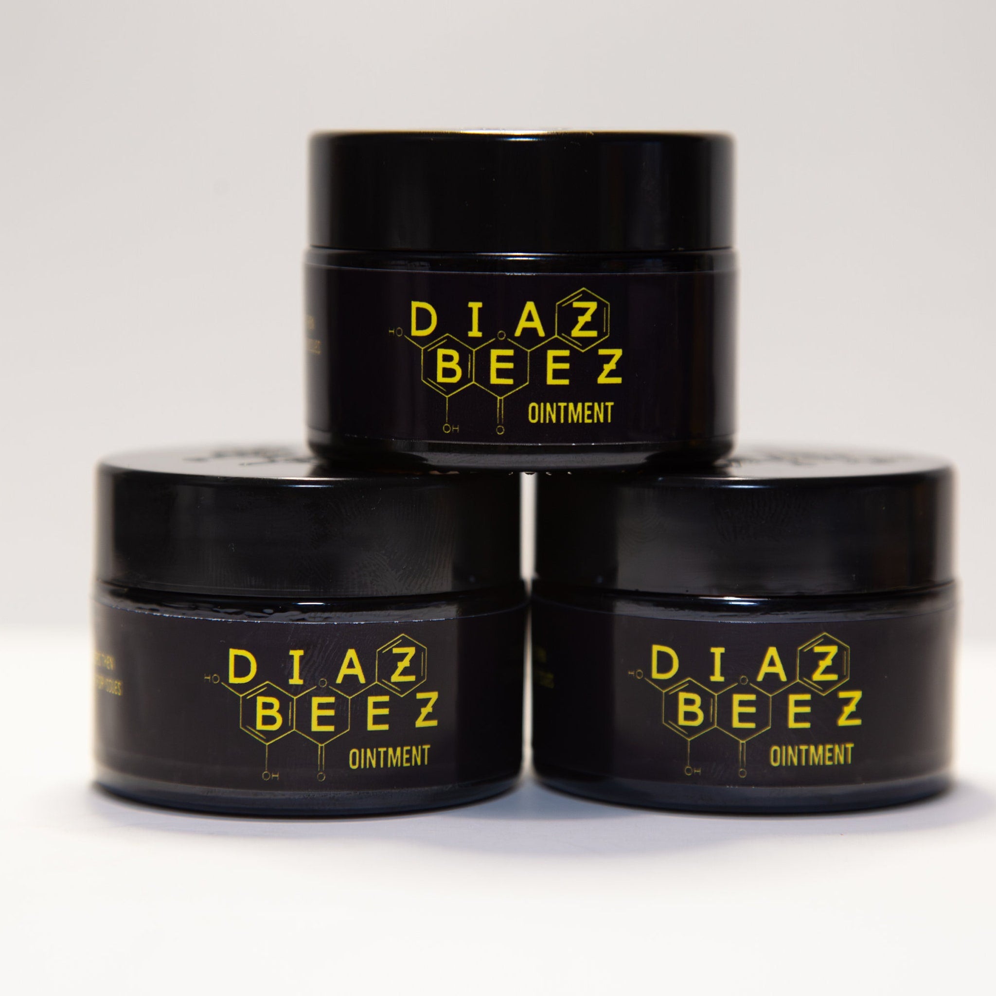 Ointment jars stacked, black containers with yellow "DIAZ BEEZ" logo and text, white background