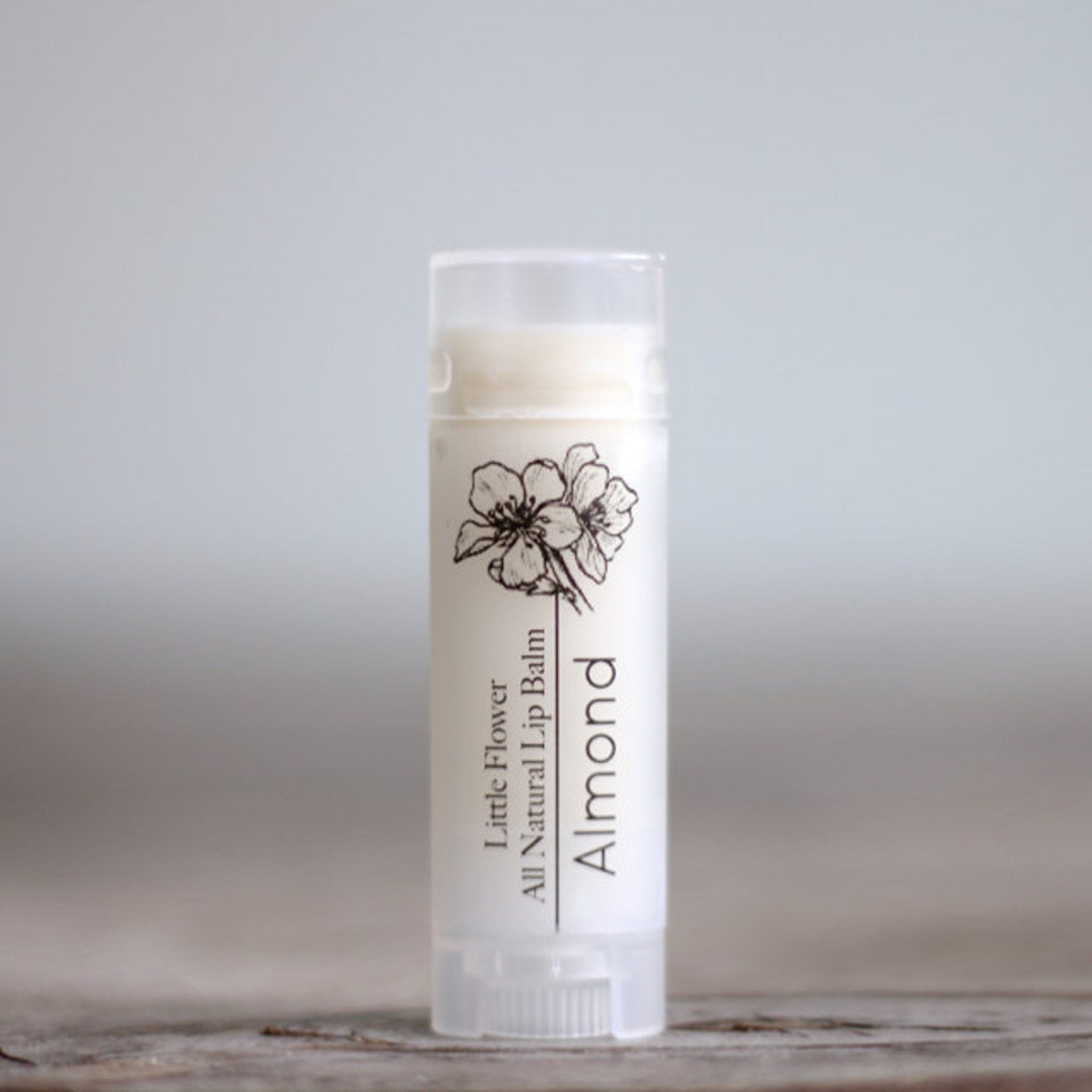 Lip balm tube with white label, black floral design, and "Almond" text.