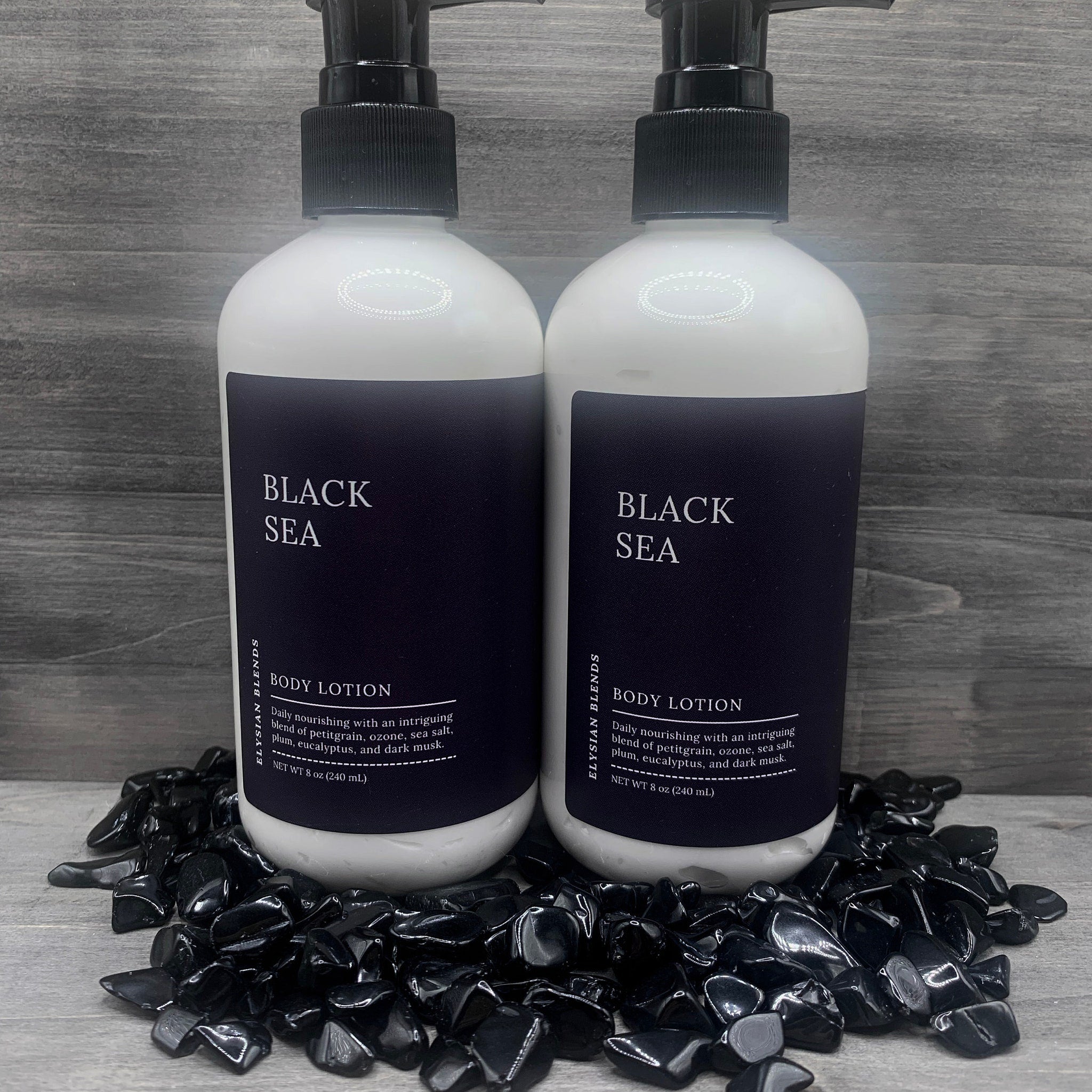 Body lotion bottles with white and black labels, black pump, and Elysian Blends branding, on black stones