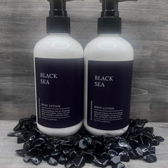 Body lotion bottles with white and black labels, black pump, and Elysian Blends branding, on black stones