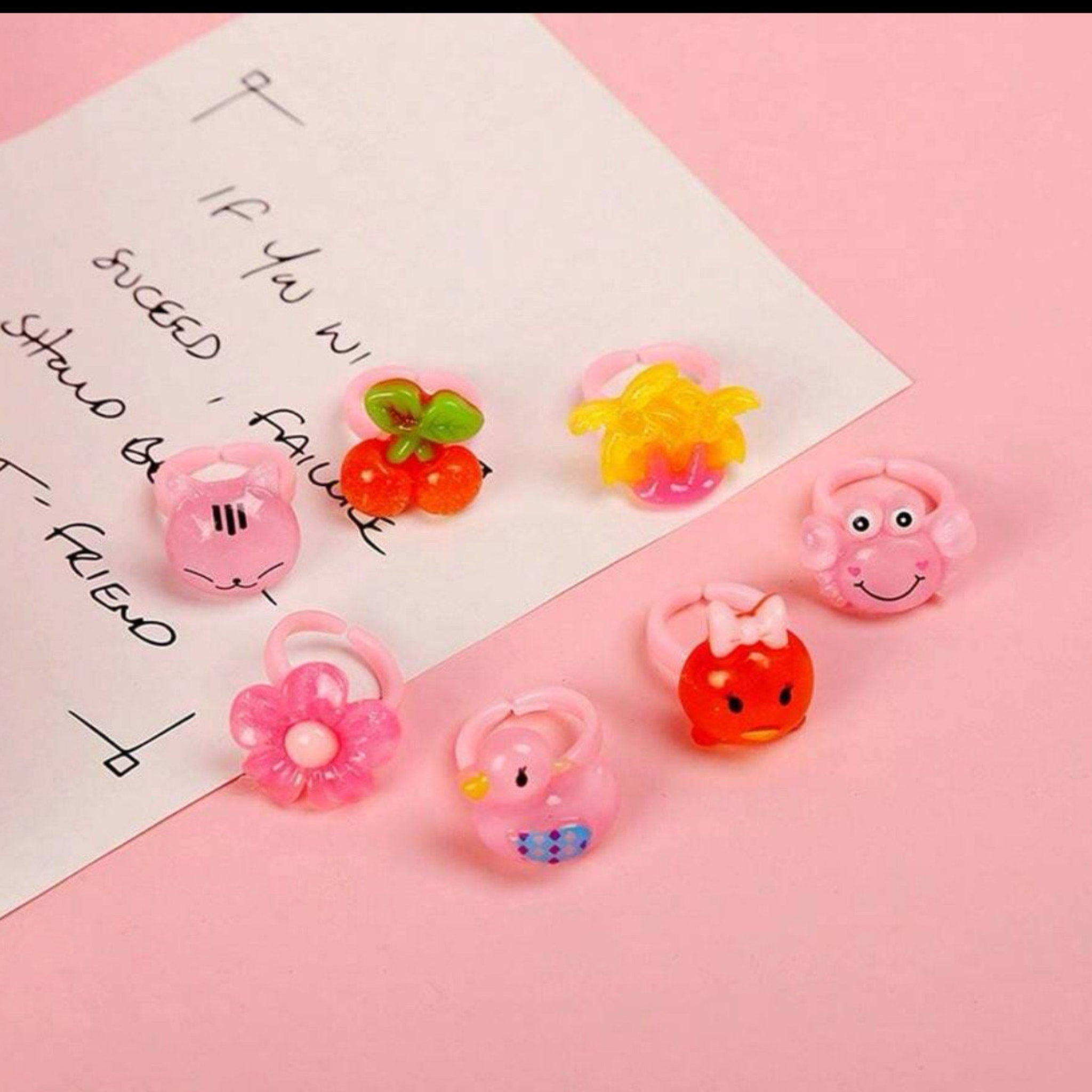 Toy rings in various colors with animal and flower designs on pink background