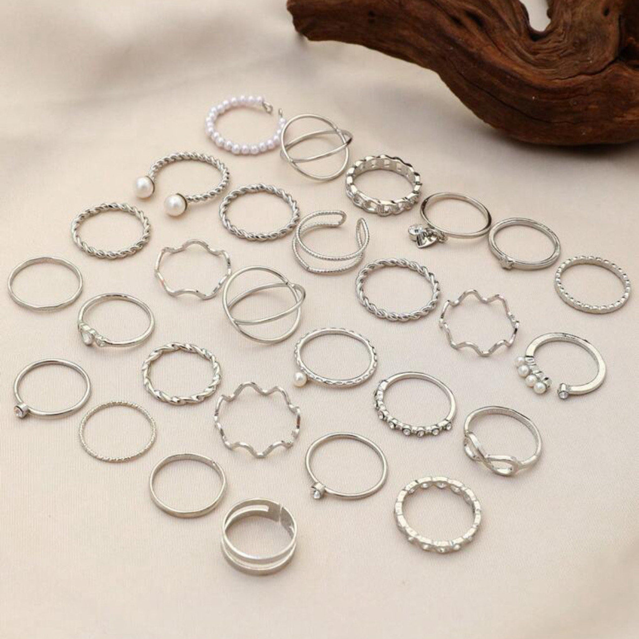 Rings set in silver metal with pearl, twisted, and geometric designs on neutral surface
