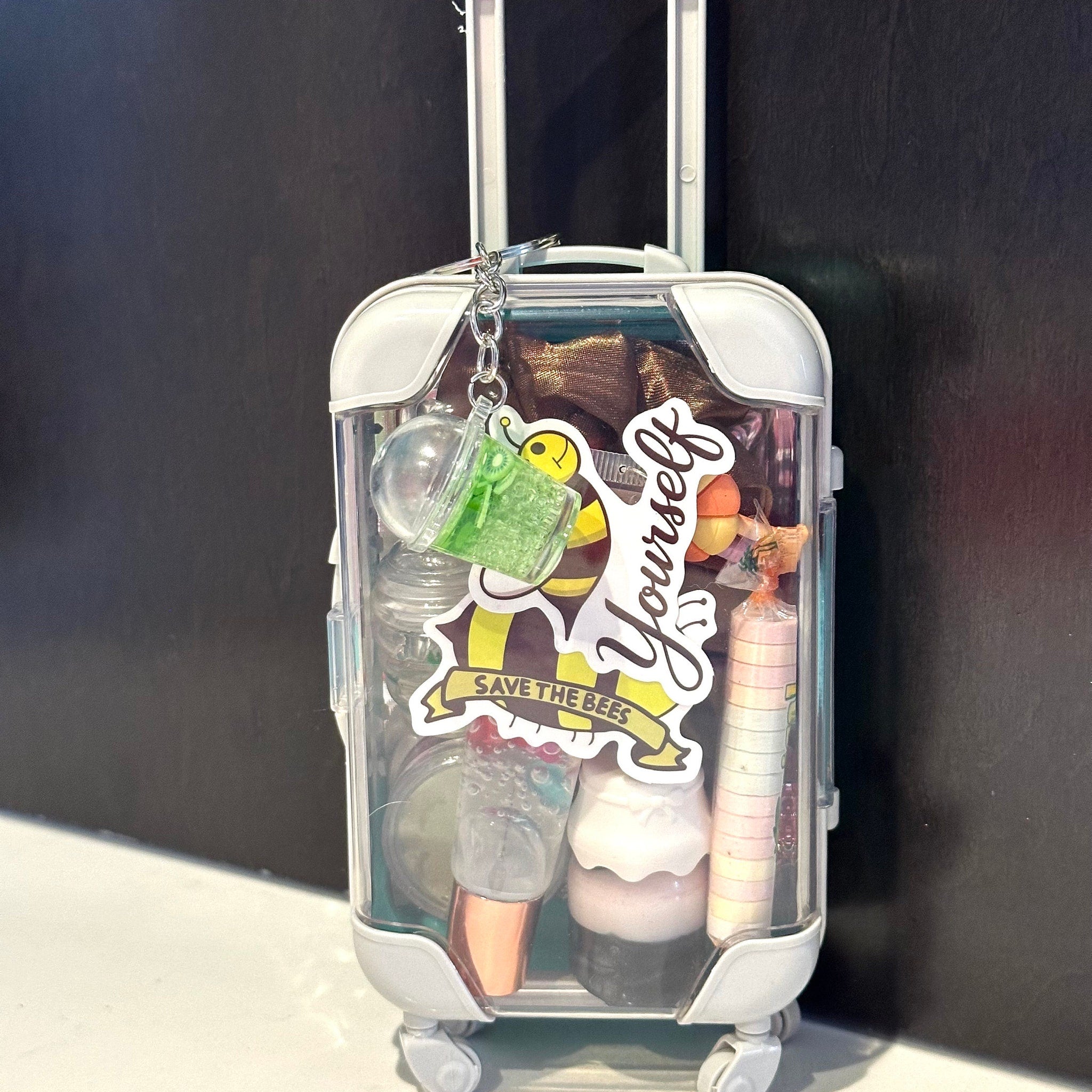 Lip gloss bundle in clear plastic suitcase with white accents and "Save the Bees" sticker
