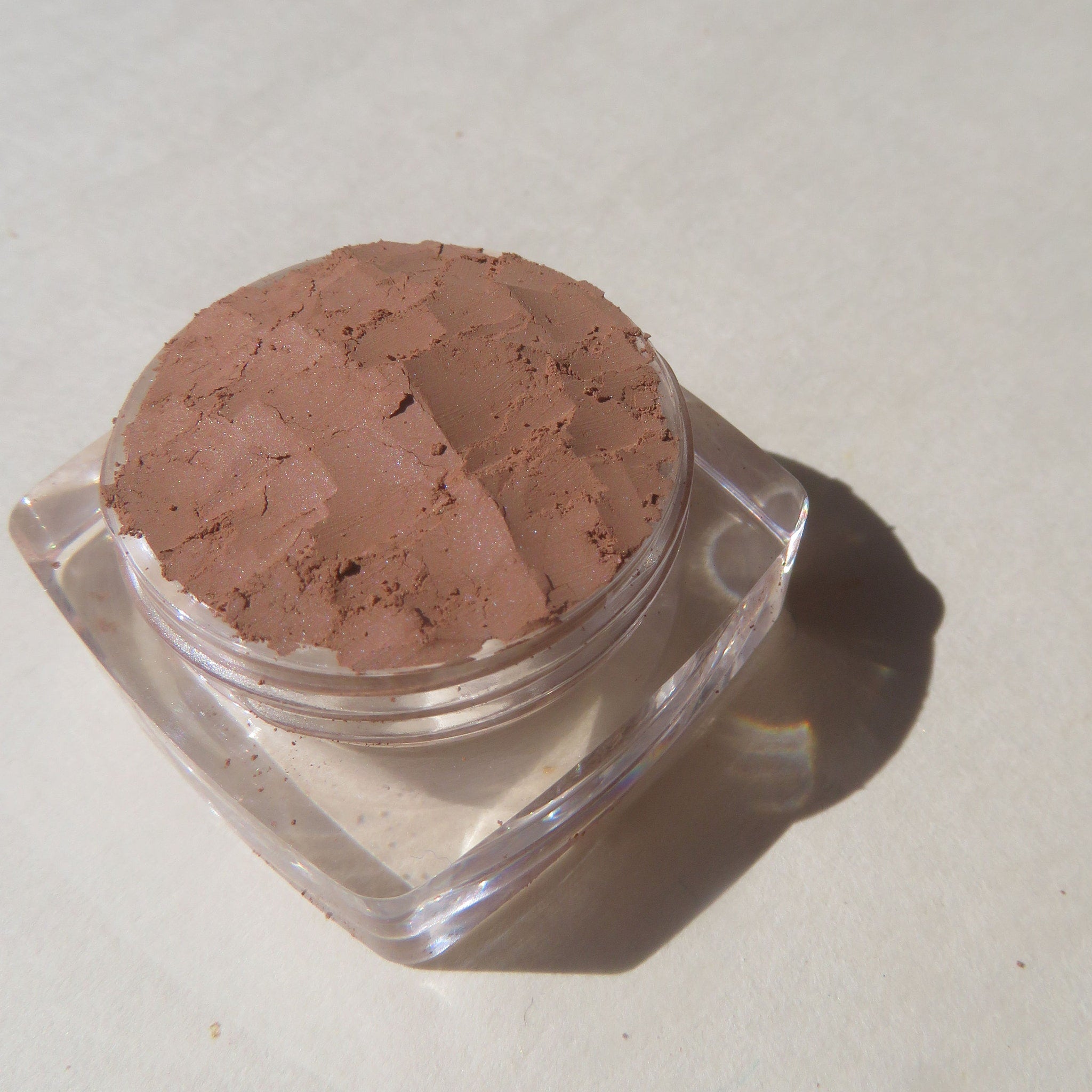 Open jar of matte brown loose powder eyeshadow with eco-friendly vegan pigments and minimalist labeling