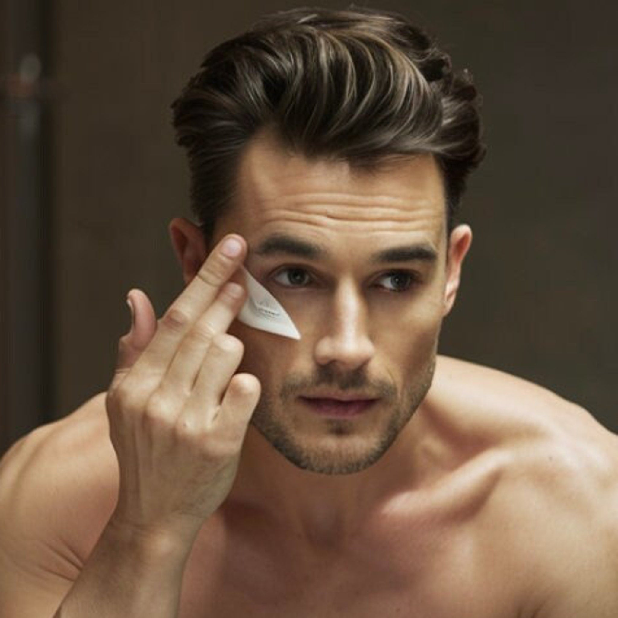 Eye cream application, man with dark hair, applying white cream to face