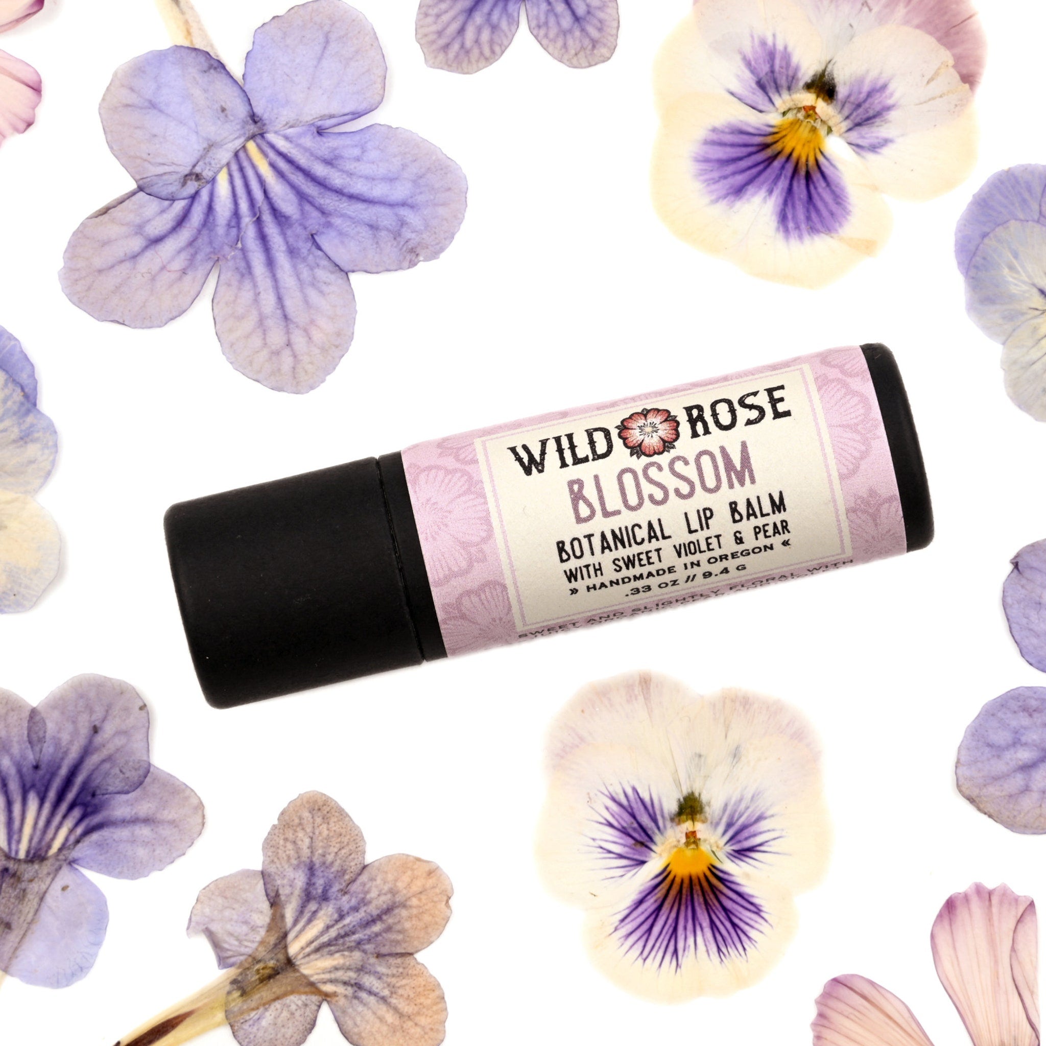 Lip balm tube with black base and floral label, surrounded by purple and white flowers