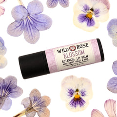 Lip balm tube with black base and floral label, surrounded by purple and white flowers