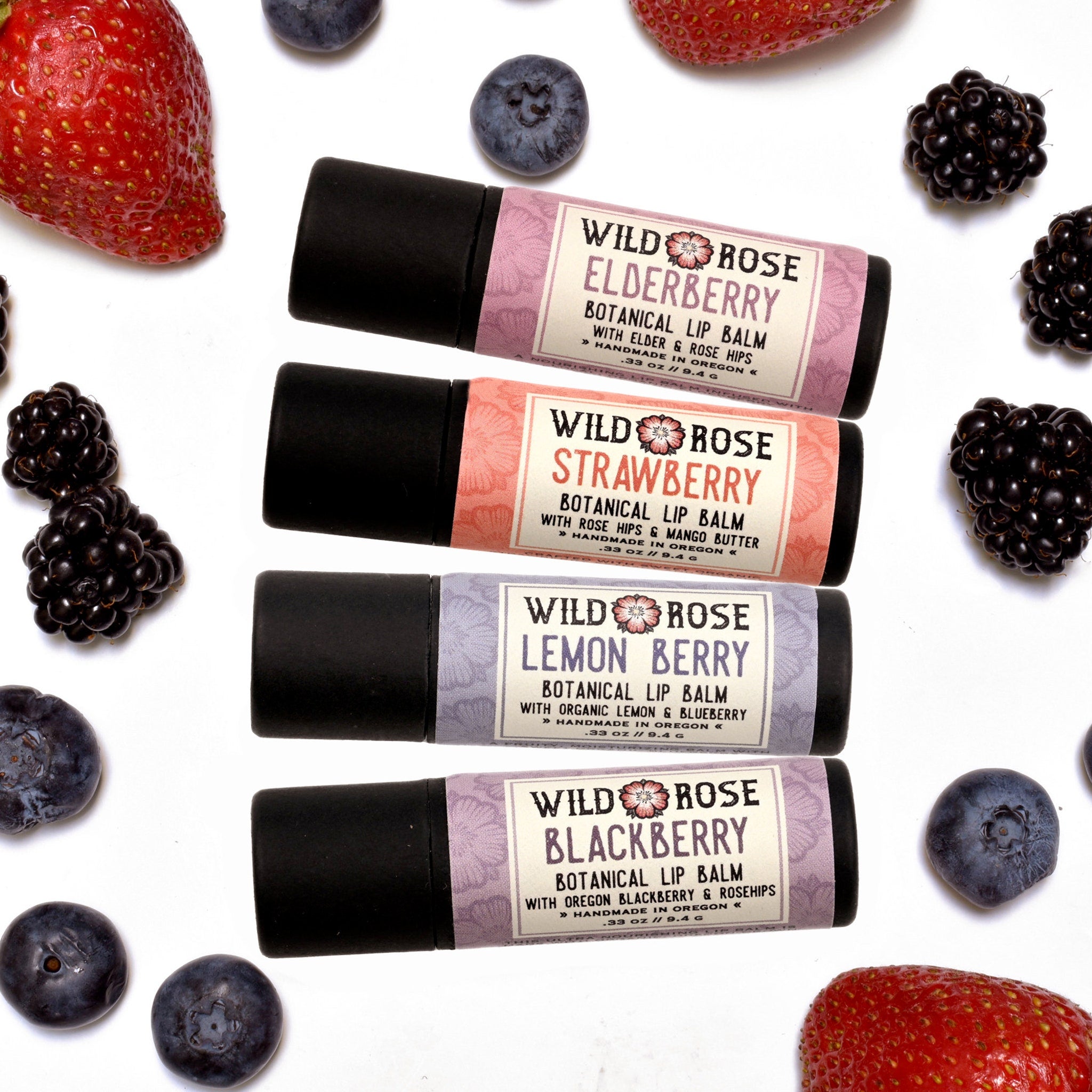Lip balm gift set with black tubes, berry labels, and fruit on white background
