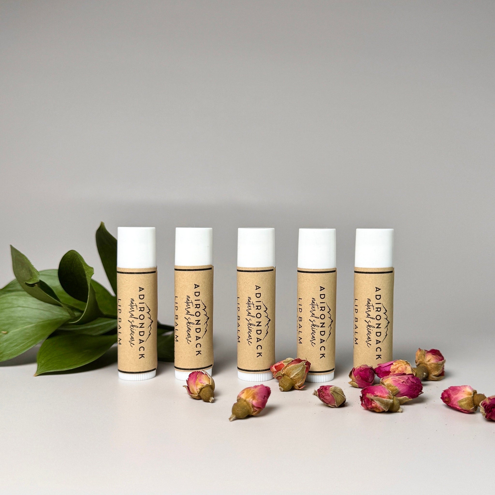 Lip balm tubes with white caps and brown labels, Adirondack Natural Skincare brand, with rose buds