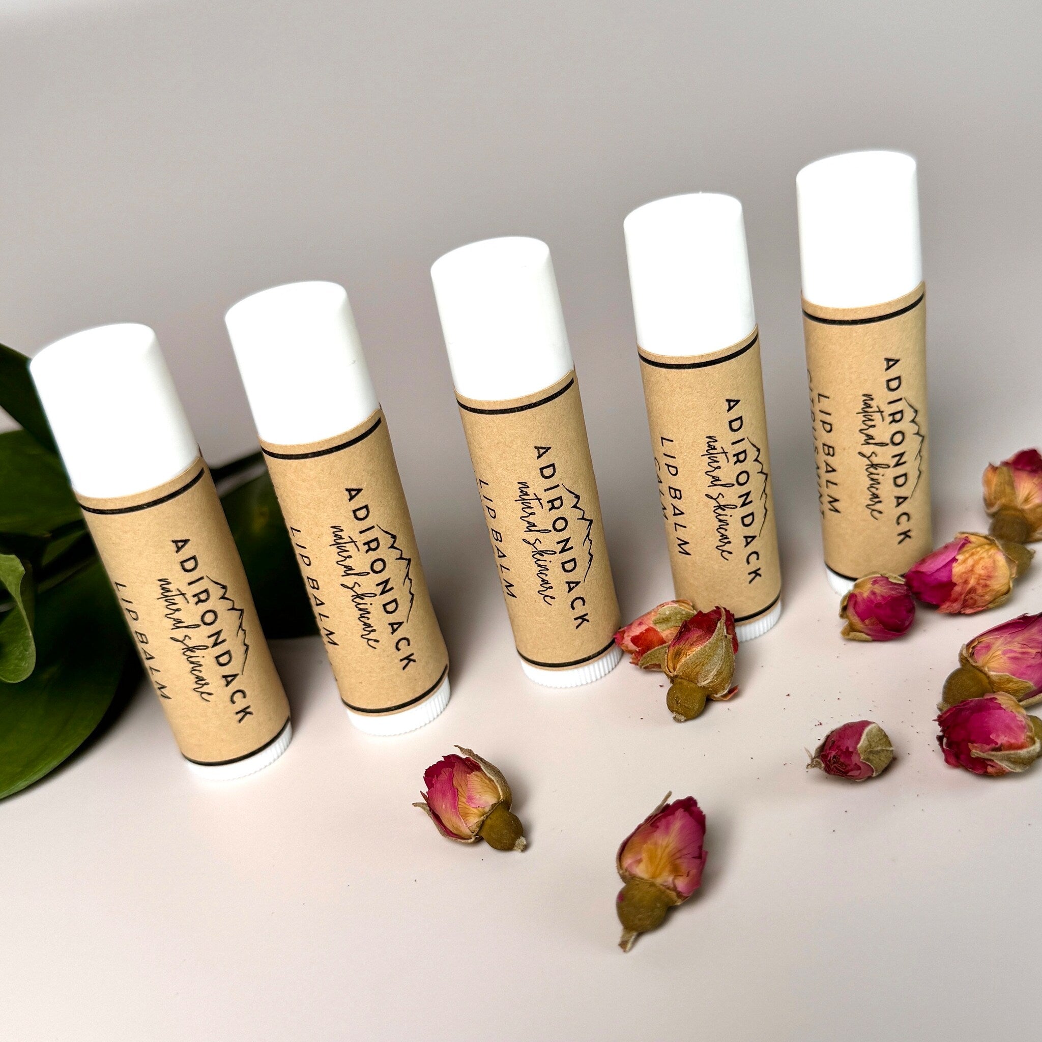 Lip balm tubes in white, brown, and black with Adirondack Natural Skincare branding and dried flowers