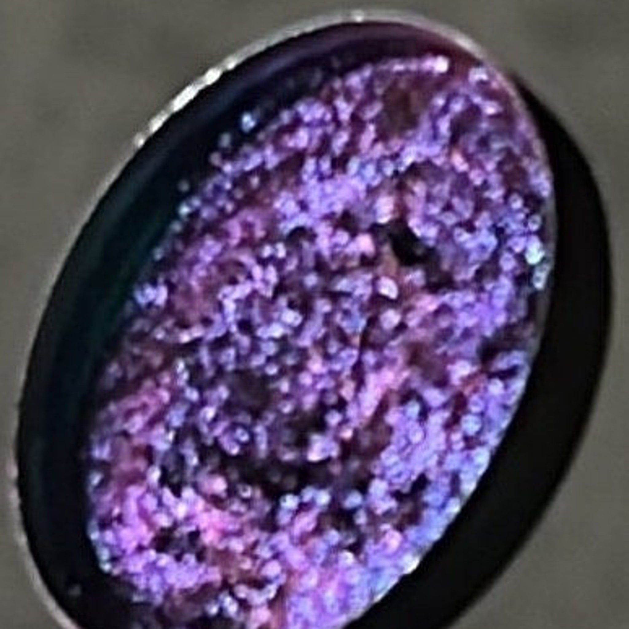 Side view of multichrome pressed eyeshadow pan showing shifting iridescent hues in compact 26mm case