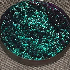 Close-up of multichrome pressed eyeshadow pan shifting between vibrant hues in a 26mm compact