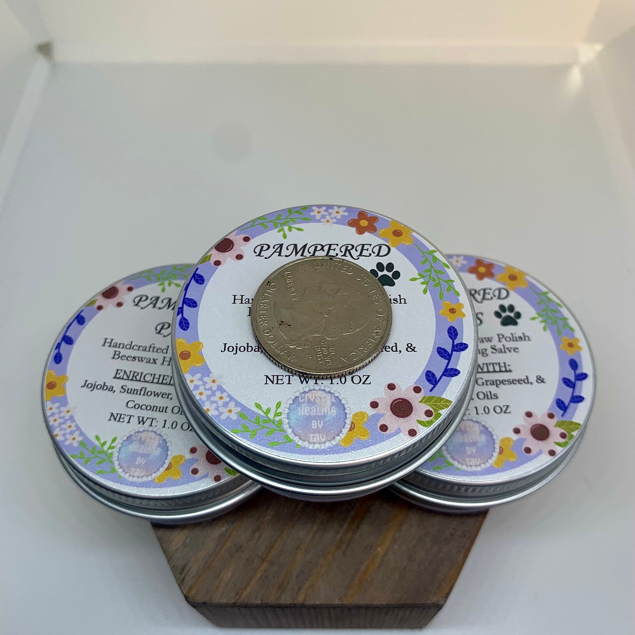 Paw polish tins with floral pattern, silver lids, and quarter coin on top, "PAMPERED" text visible