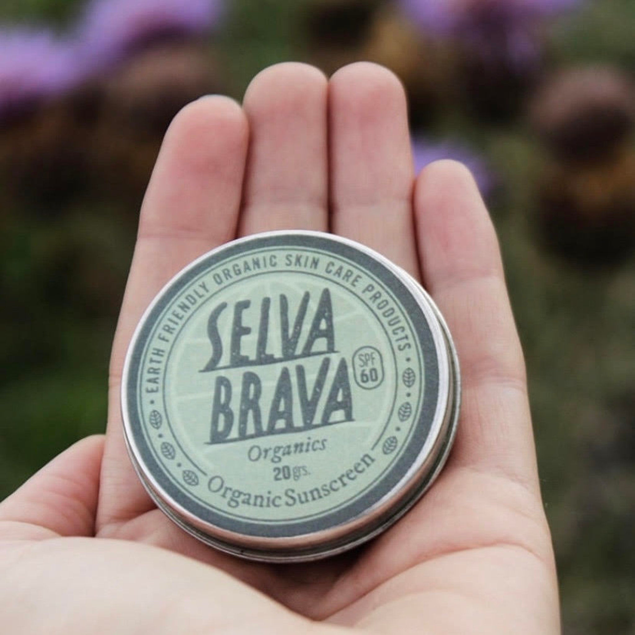 Organic sunscreen tin, green and silver, held in hand with Selva Brava text visible