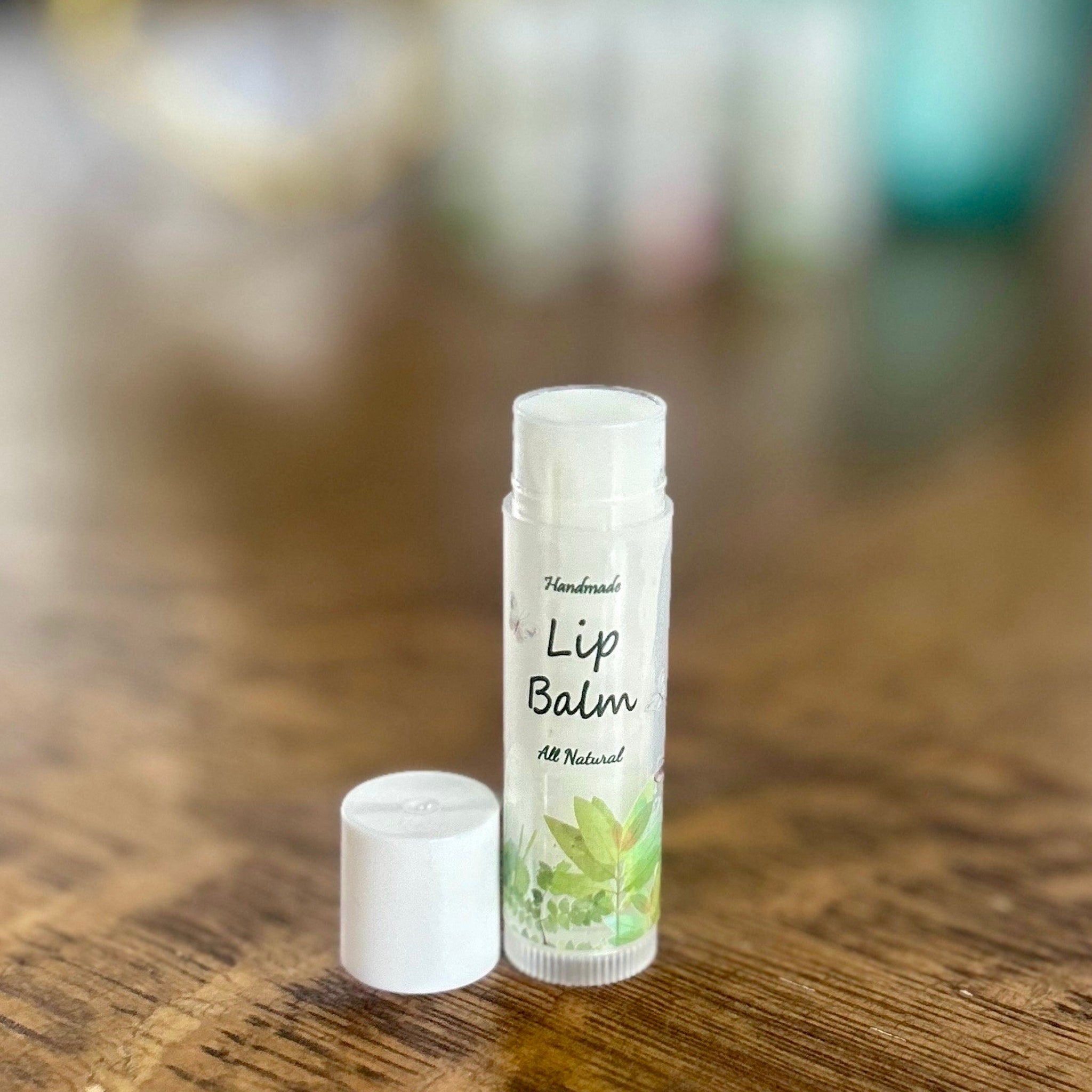 Lip balm tube with white cap, clear label, and green leaf design on wooden surface
