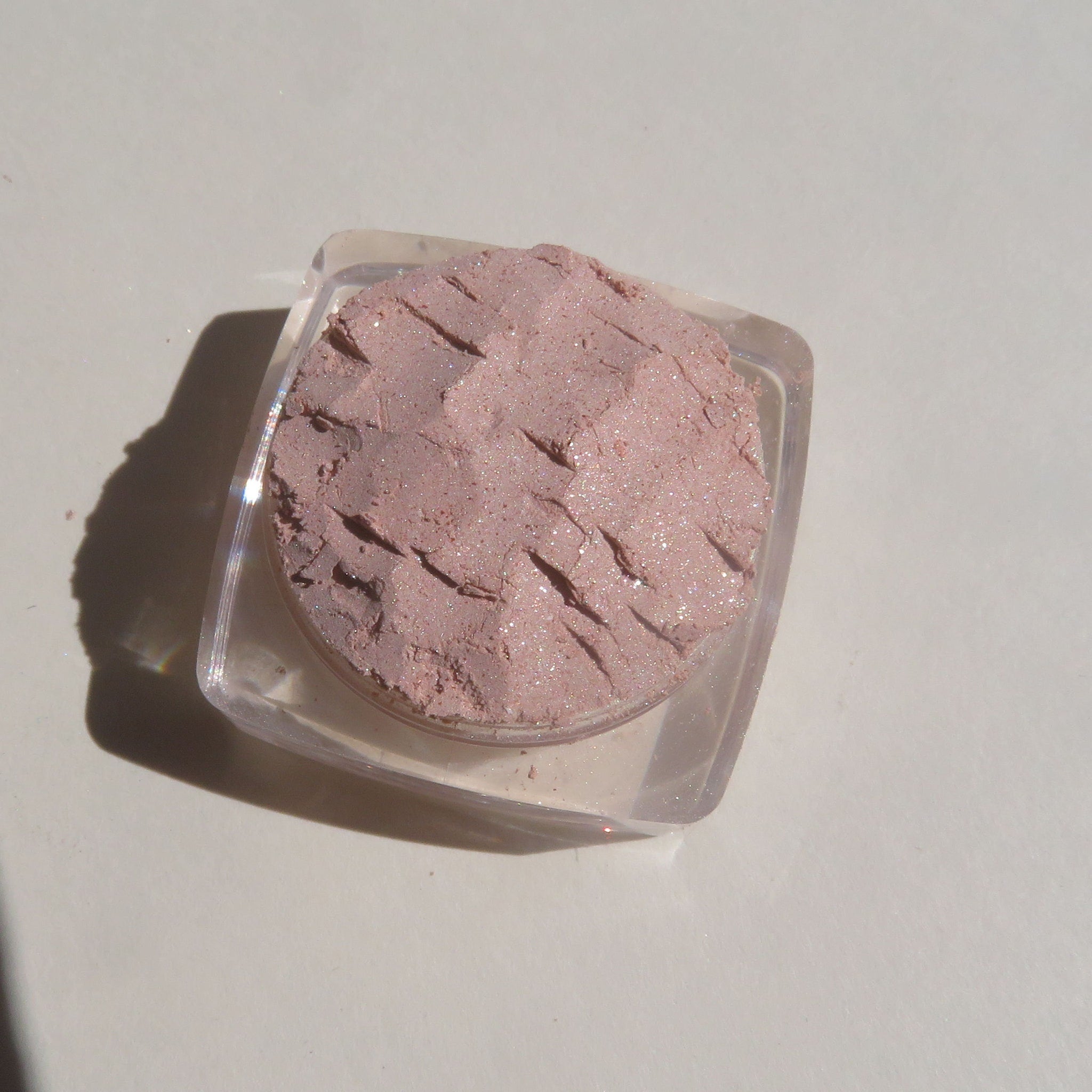 Side view of loose mineral eyeshadow in frosty golden champagne with shimmering beige-brown particles