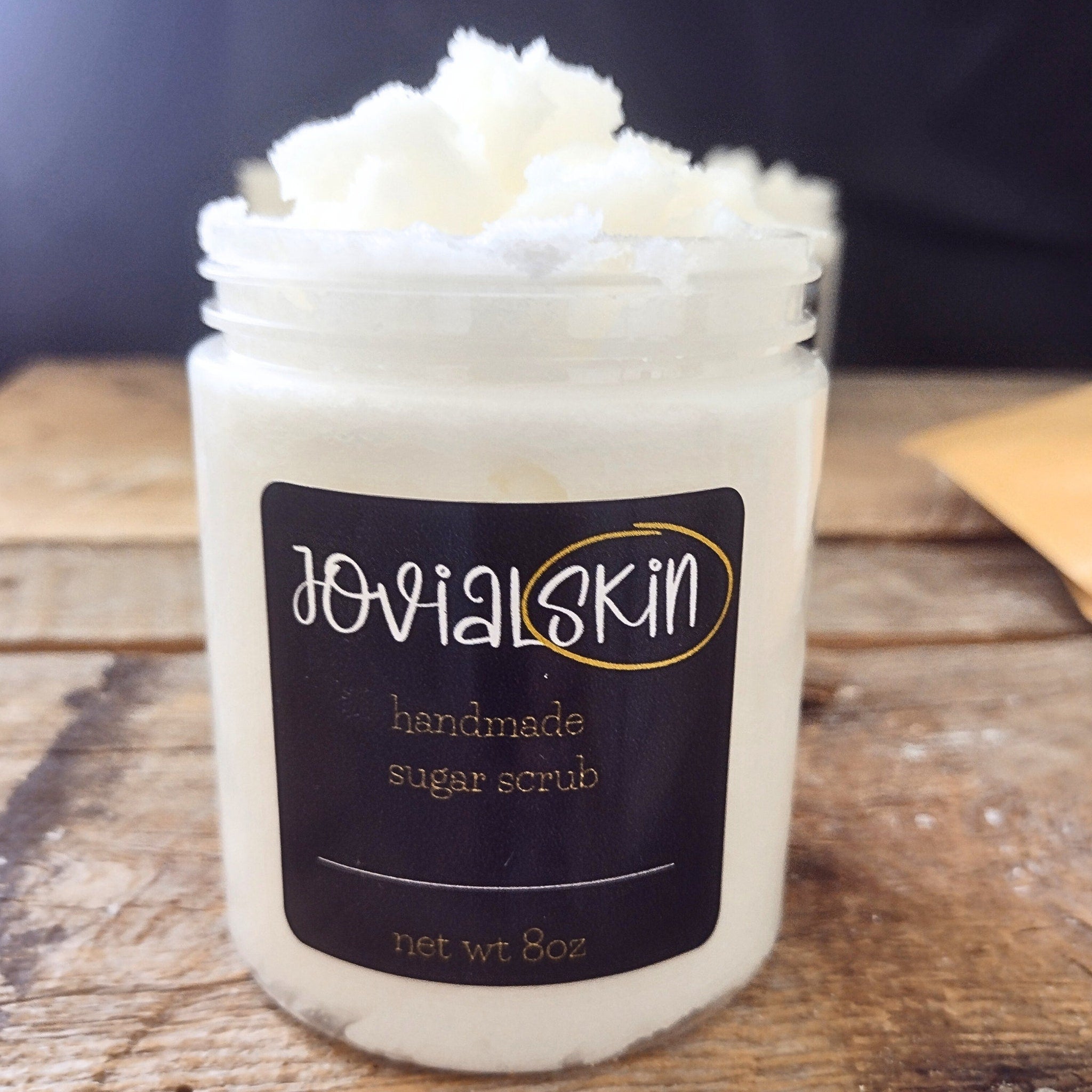 Sugar scrub in a clear jar with white scrub, black label, and JovialSkin brand name visible.
