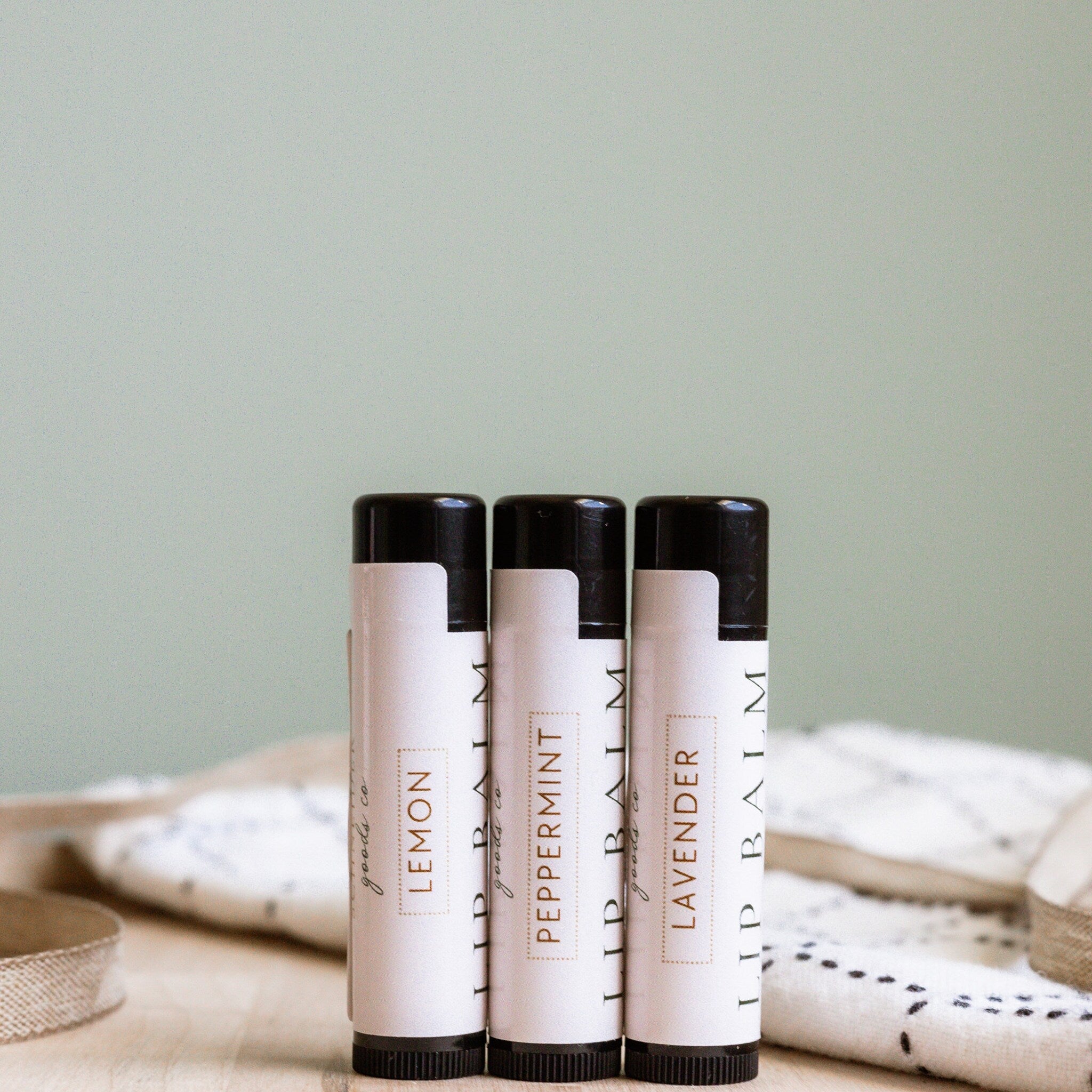 Lip balm tubes with black caps and white labels, goods co brand, on wooden surface
