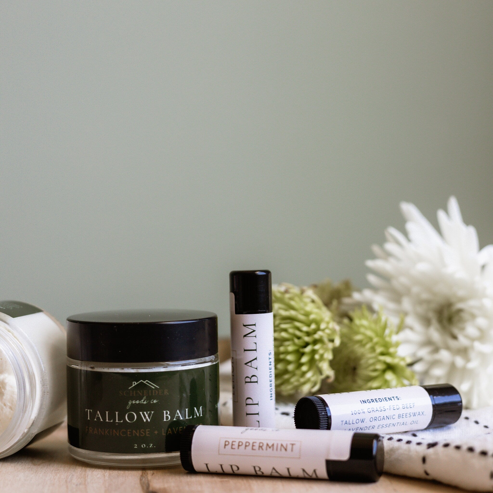 Lip balm tubes and jar with black lids and white labels, on a wooden surface with flowers