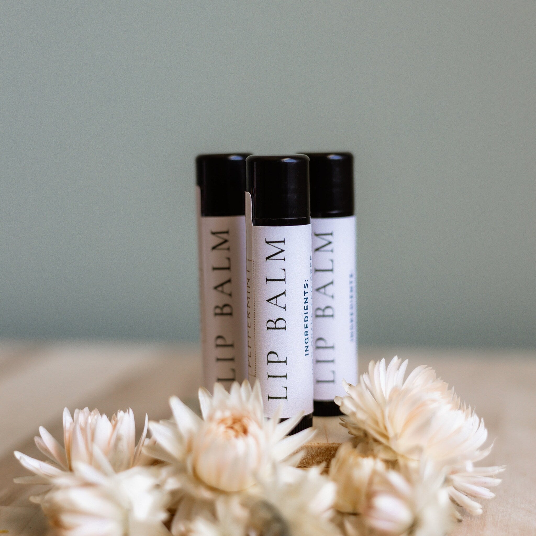 Lip balm tubes with black caps and white labels, displayed with white flowers