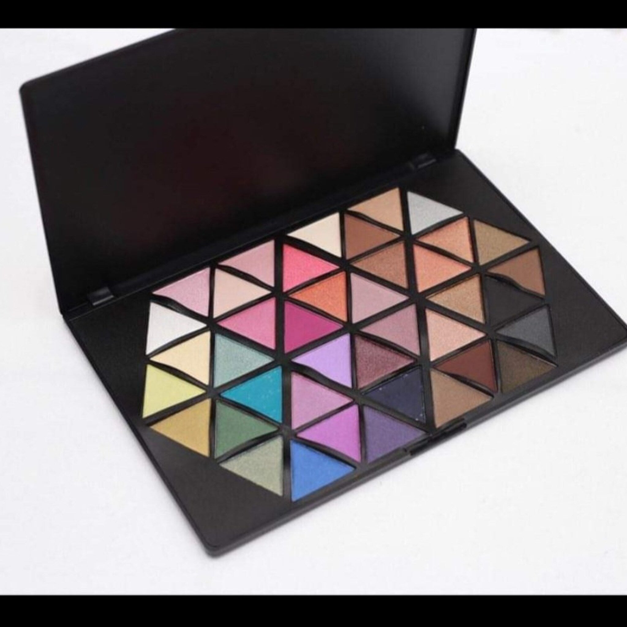 Eyeshadow palette with multiple colors in a black geometric case, open on white background.