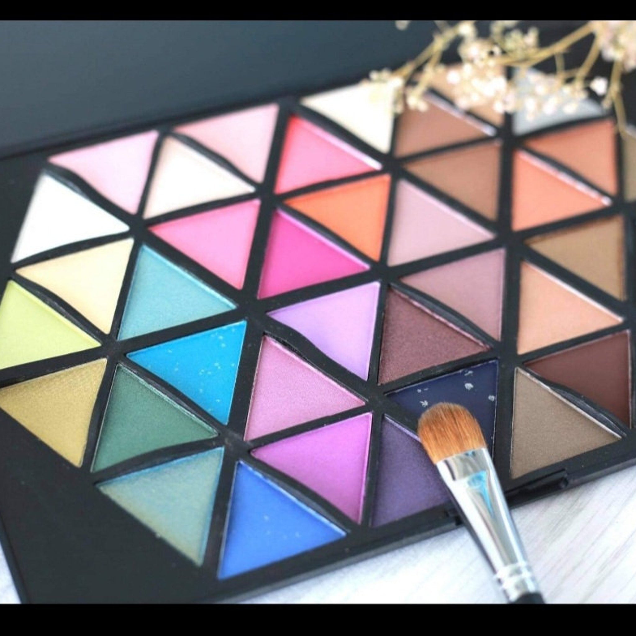 Side view of Vivid Cosmetics eyeshadow palette showing sleek black case and vibrant color assortment