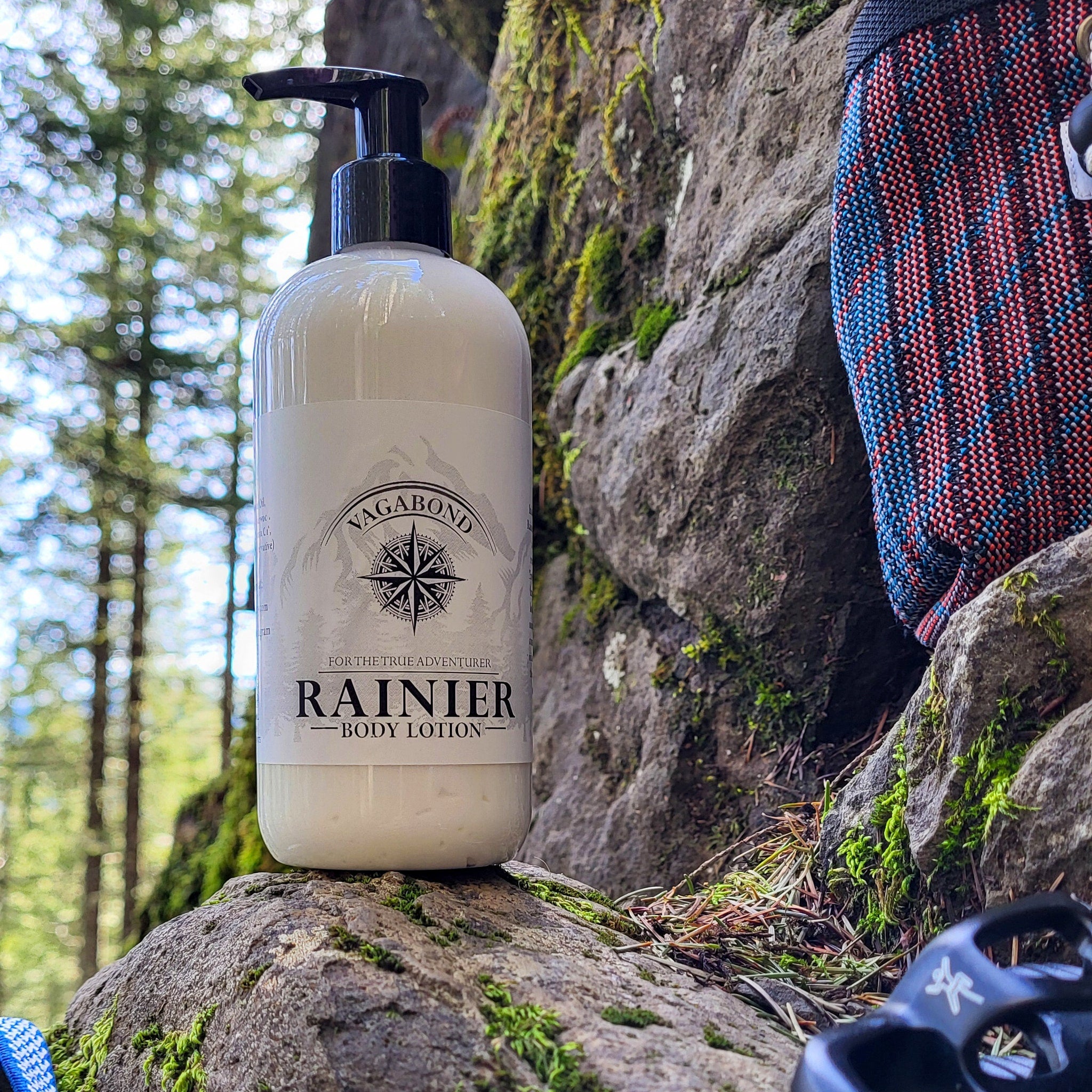 Body lotion bottle, white, black pump top, with "RAINIER" text, on rock outdoors