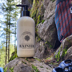 Body lotion bottle, white, black pump top, with "RAINIER" text, on rock outdoors