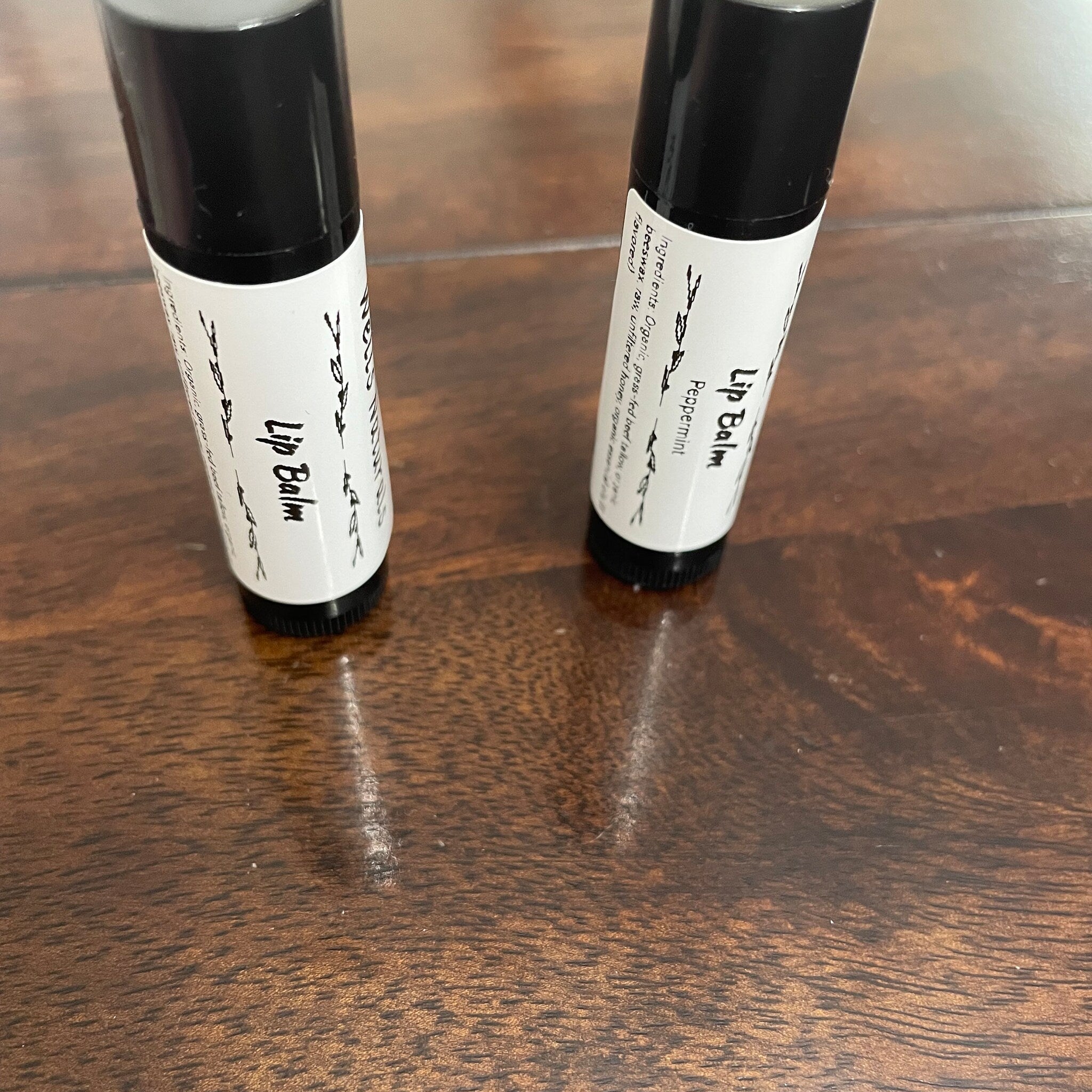 Lip balm tubes with black caps and white labels, on wooden surface