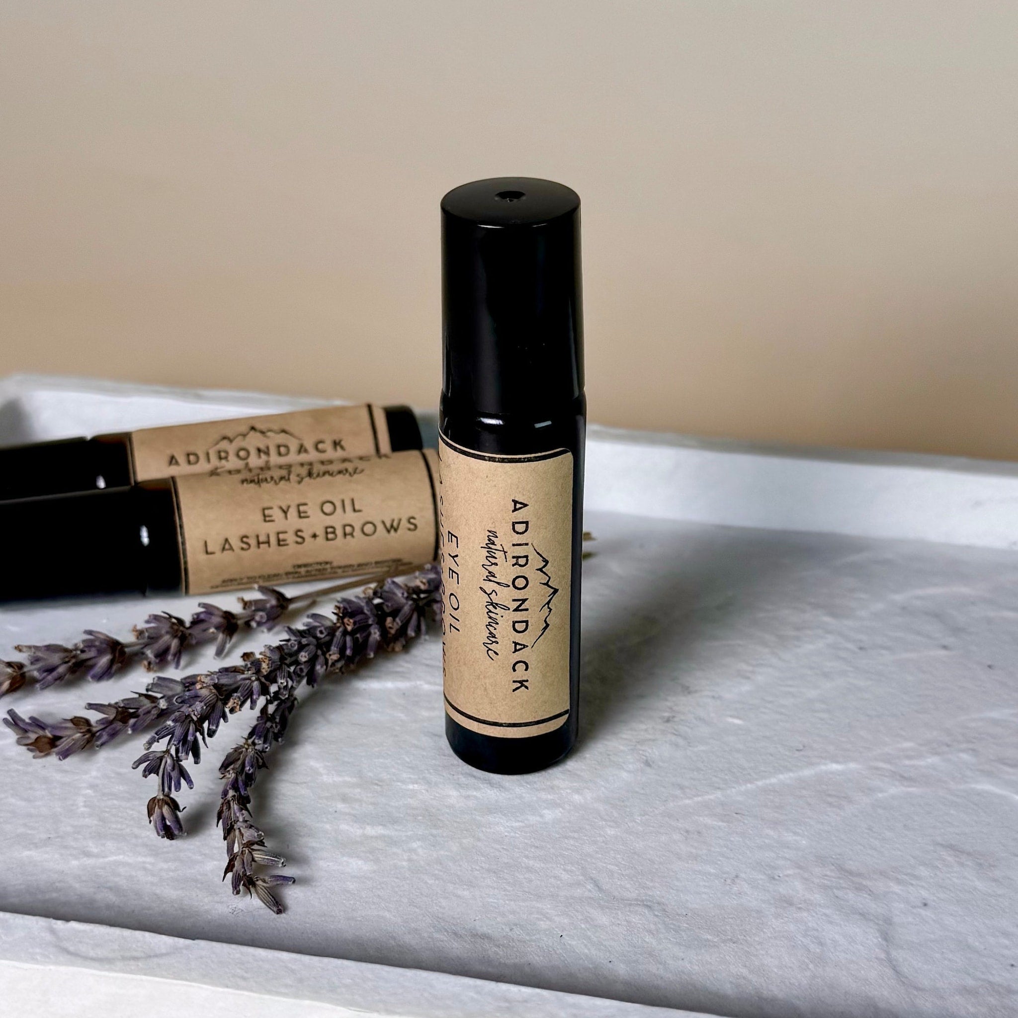 Eye oil roll-on bottle with black cap and label, on a white tray with lavender