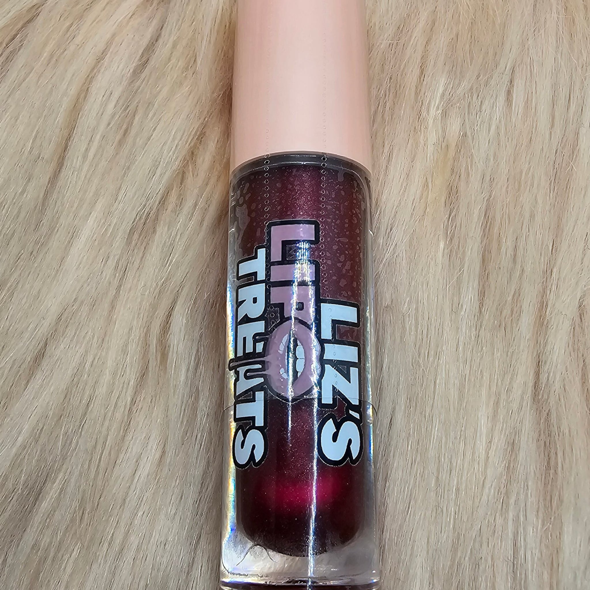 Lip gloss in a clear tube with a pink cap, dark red color, and Lipz Treats label on a furry background