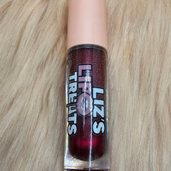 Lip gloss in a clear tube with a pink cap, dark red color, and Lipz Treats label on a furry background