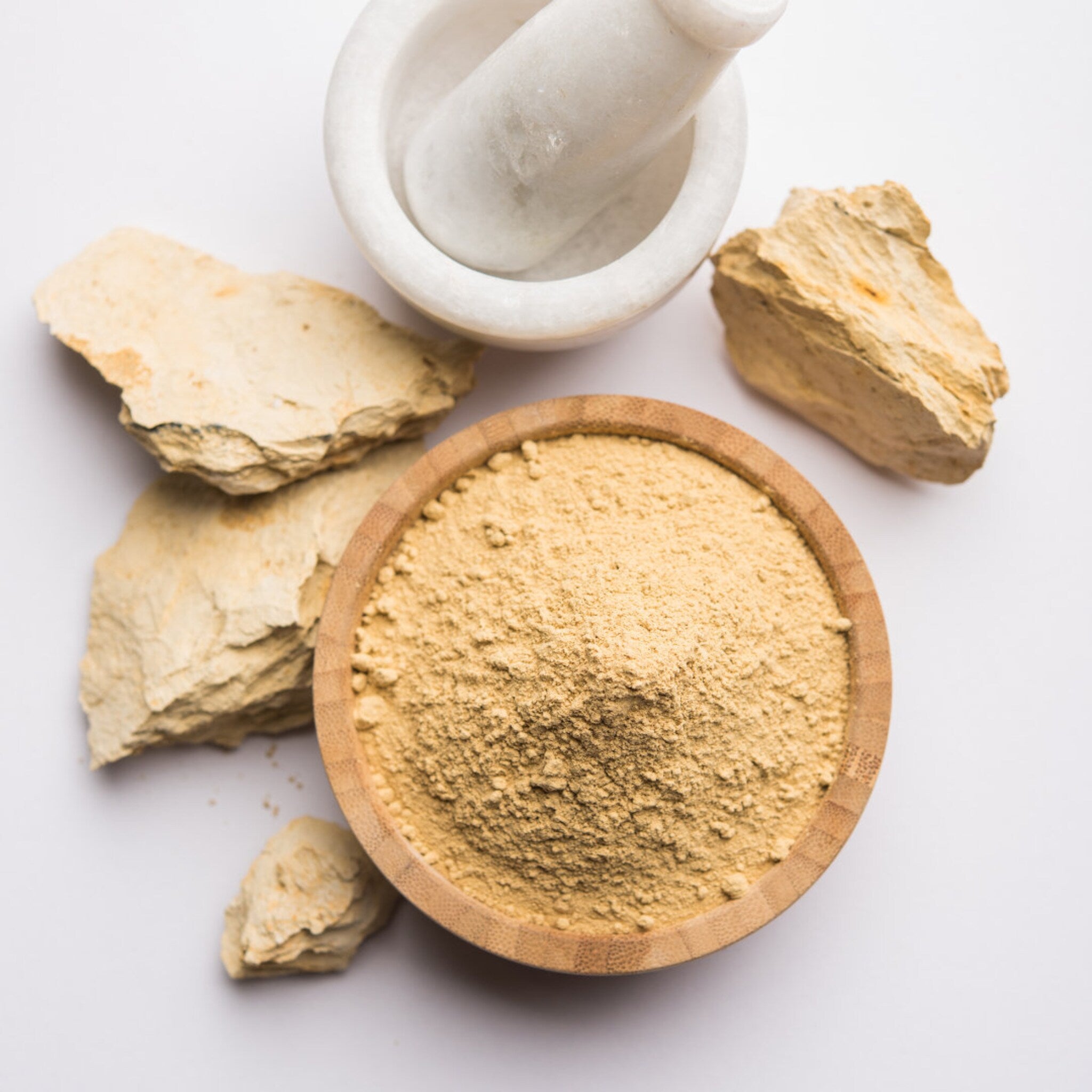 Clay powder in a wooden bowl with beige powder and stone pieces with a white mortar and pestle