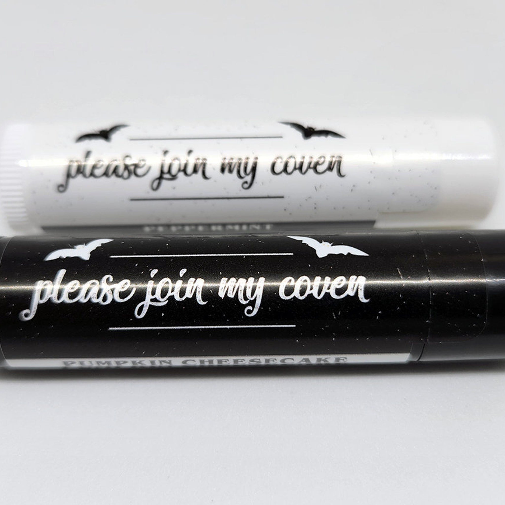 Lip balm tubes, black and white with bats, "please join my coven" text, close-up view