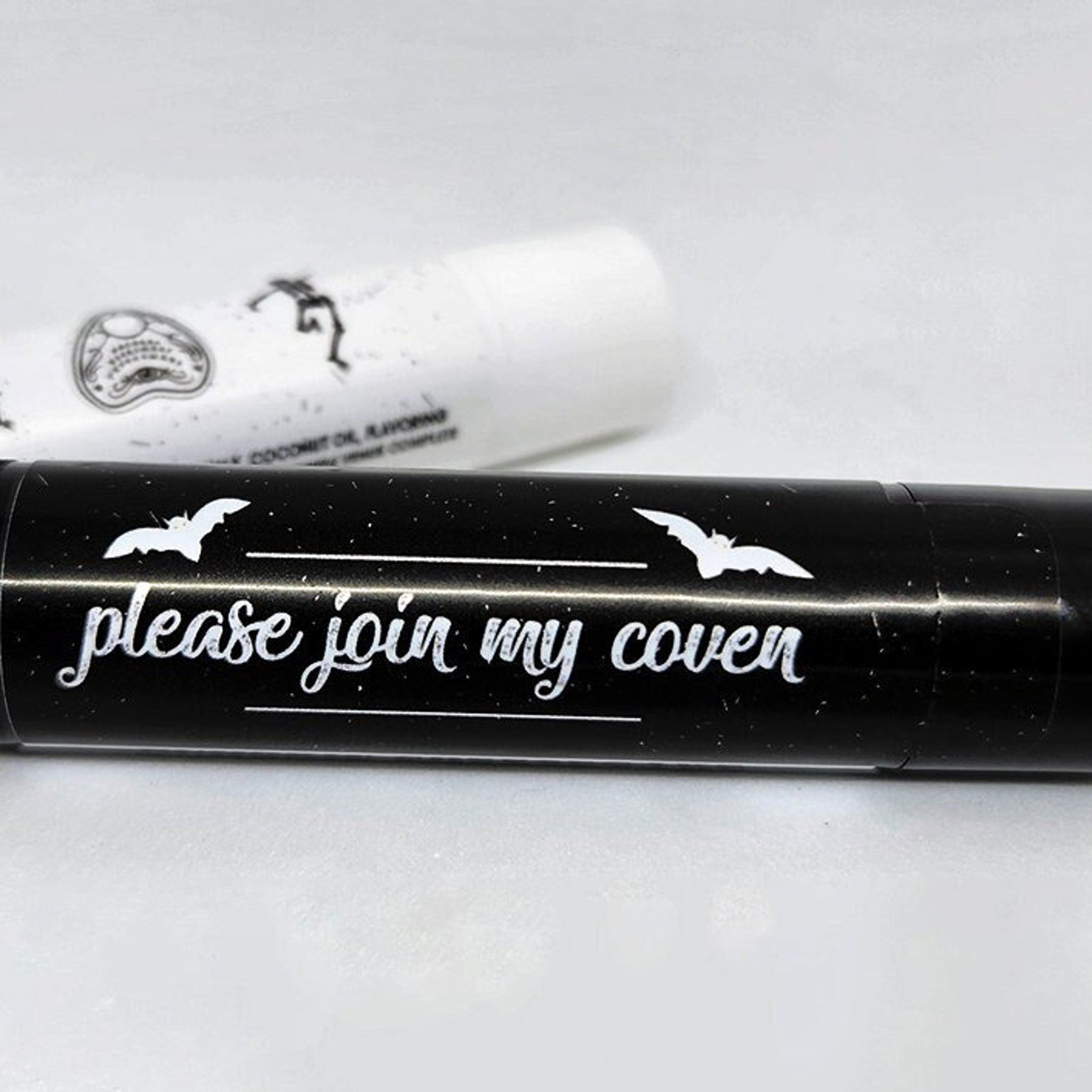 Black lipstick tube with white bat illustrations and text "please join my coven" on black background