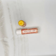 Lip balm tubes with white and patterned labels, open jar with yellow balm, Hue & Lather brand visible