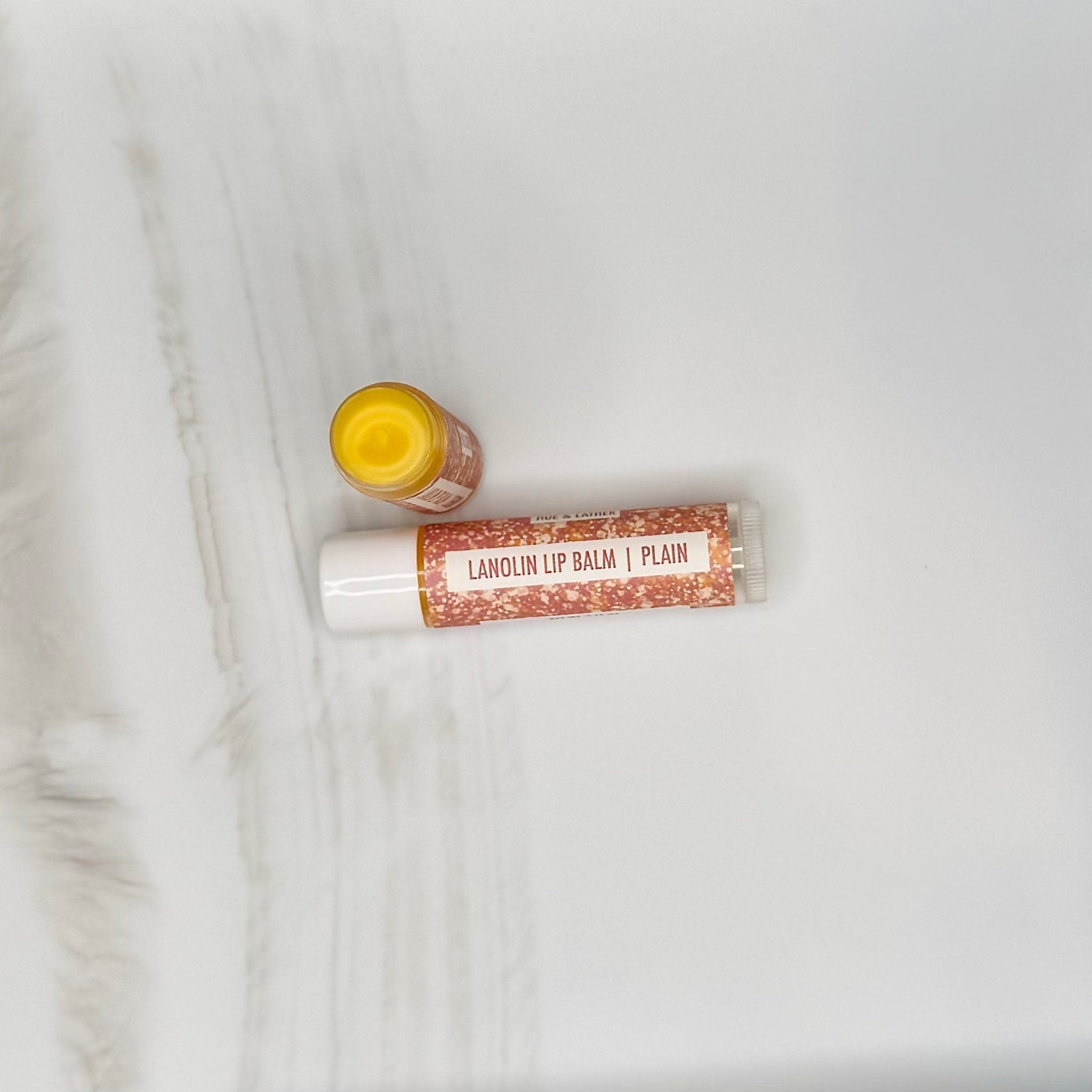 Lanolin lip balm, white tube with orange speckled pattern, yellow balm visible